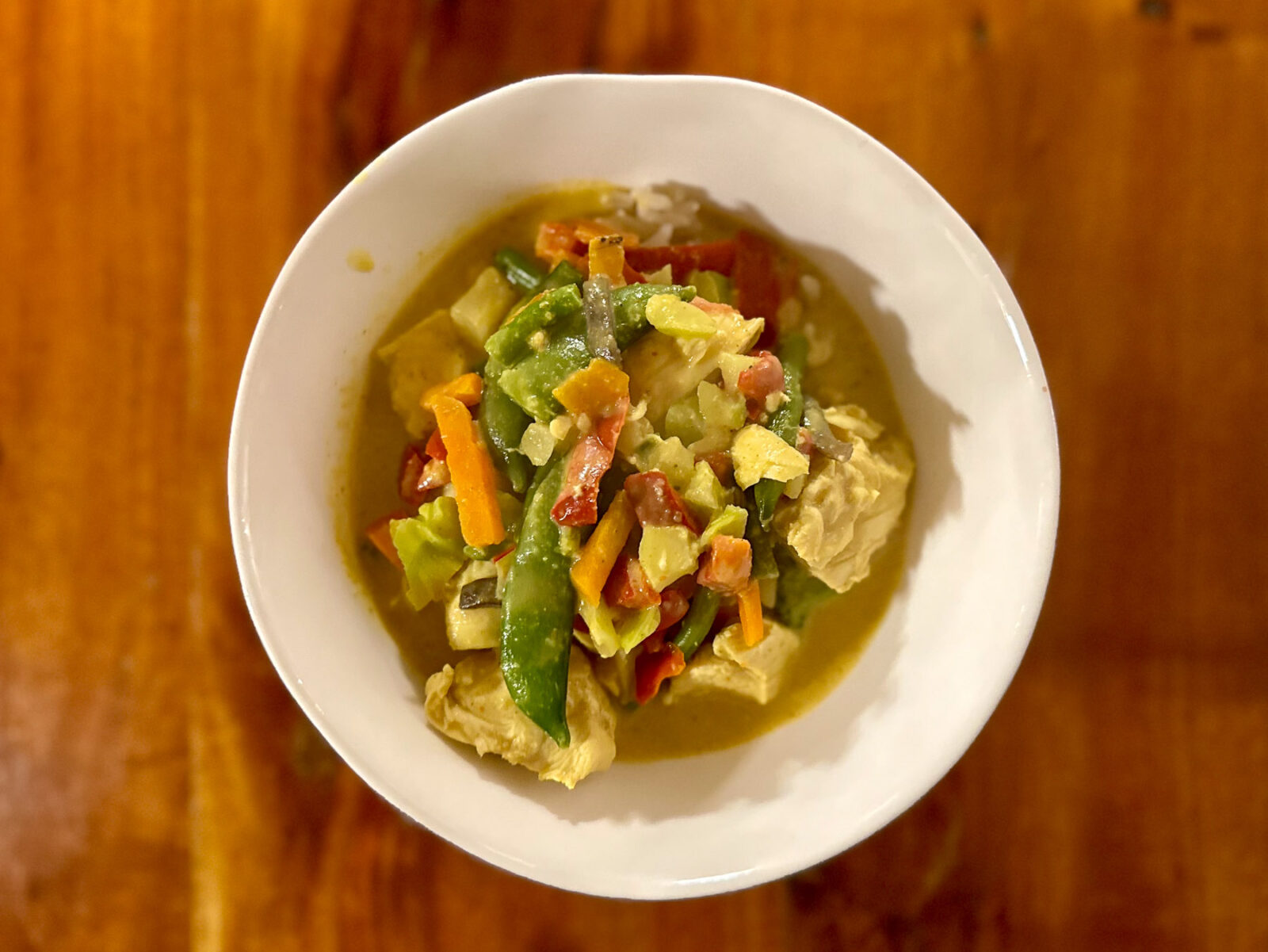 Overhead view of a bowl of Thai yellow curry with chicken, mixed vegetables, and brown jasmine rice in a creamy curry sauce.