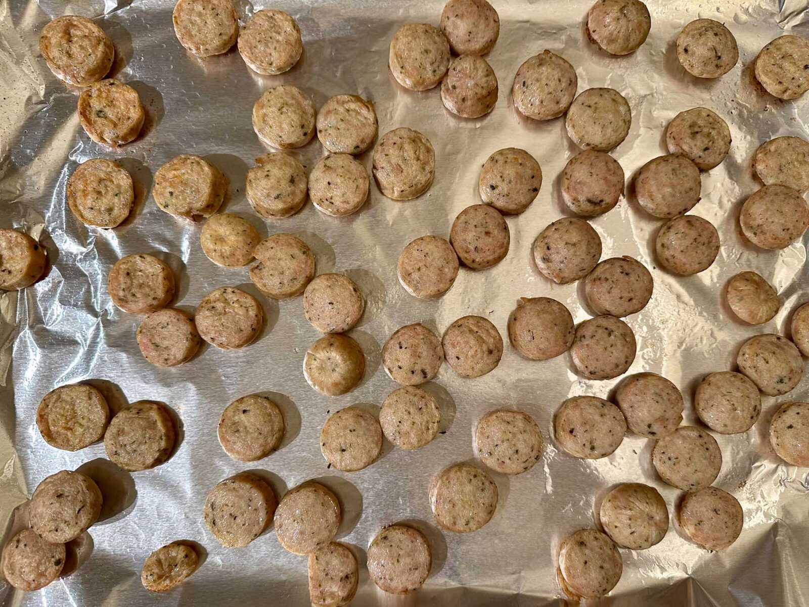 Roasted sliced chicken sausage rounds spread on a foil-lined baking sheet.