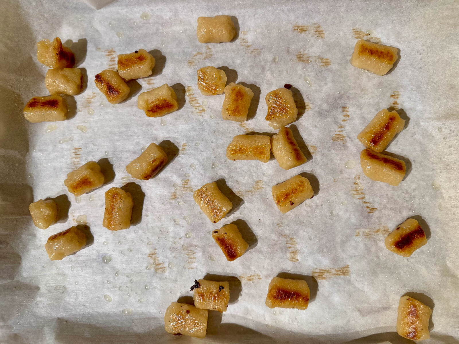 Close-up of roasted cauliflower gnocchi on parchment paper, showing golden brown and crispy edges.