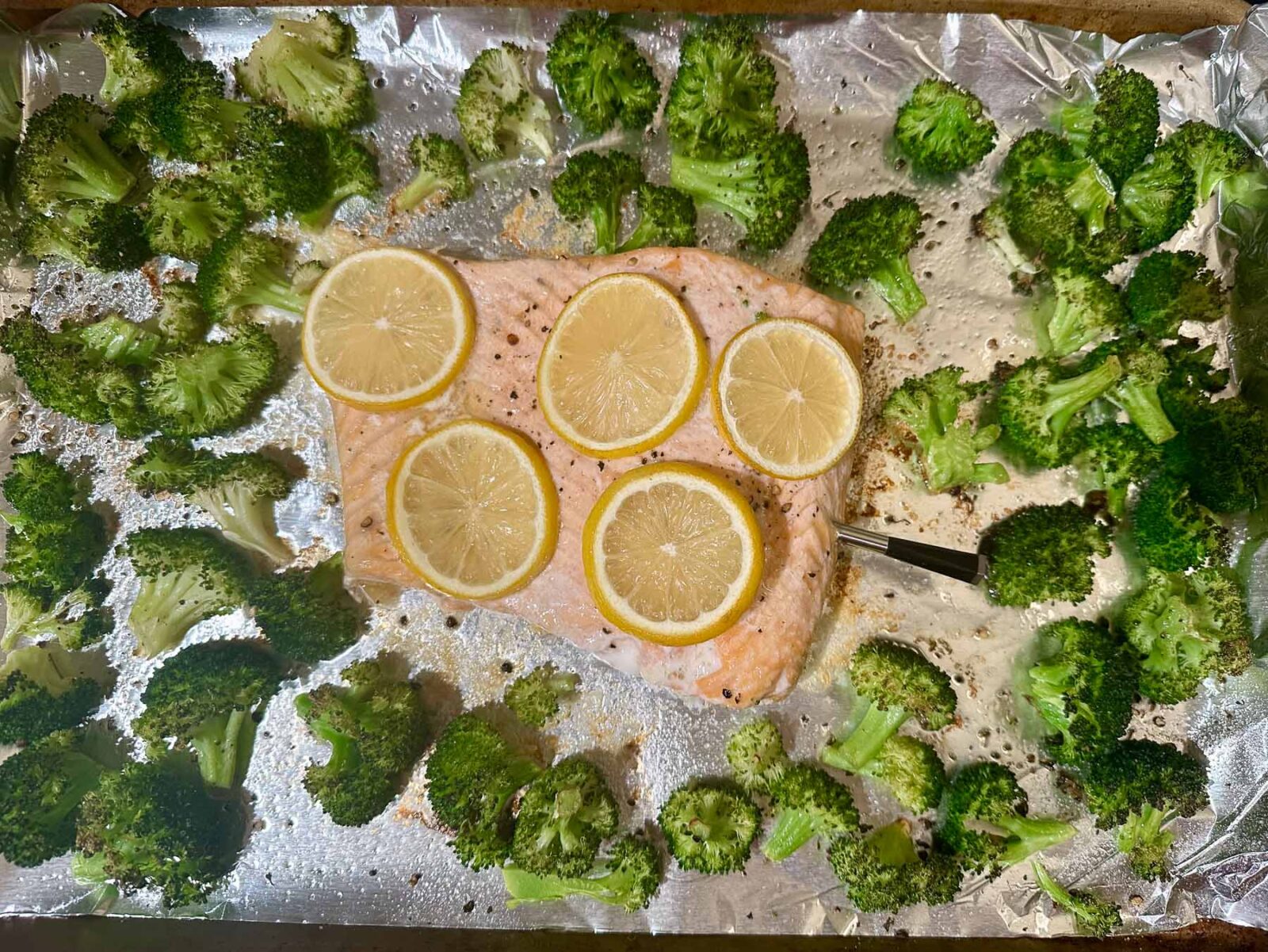 Fully cooked sheet pan with roasted salmon and charred broccoli, showing caramelized edges and cooked-through lemon-topped salmon.