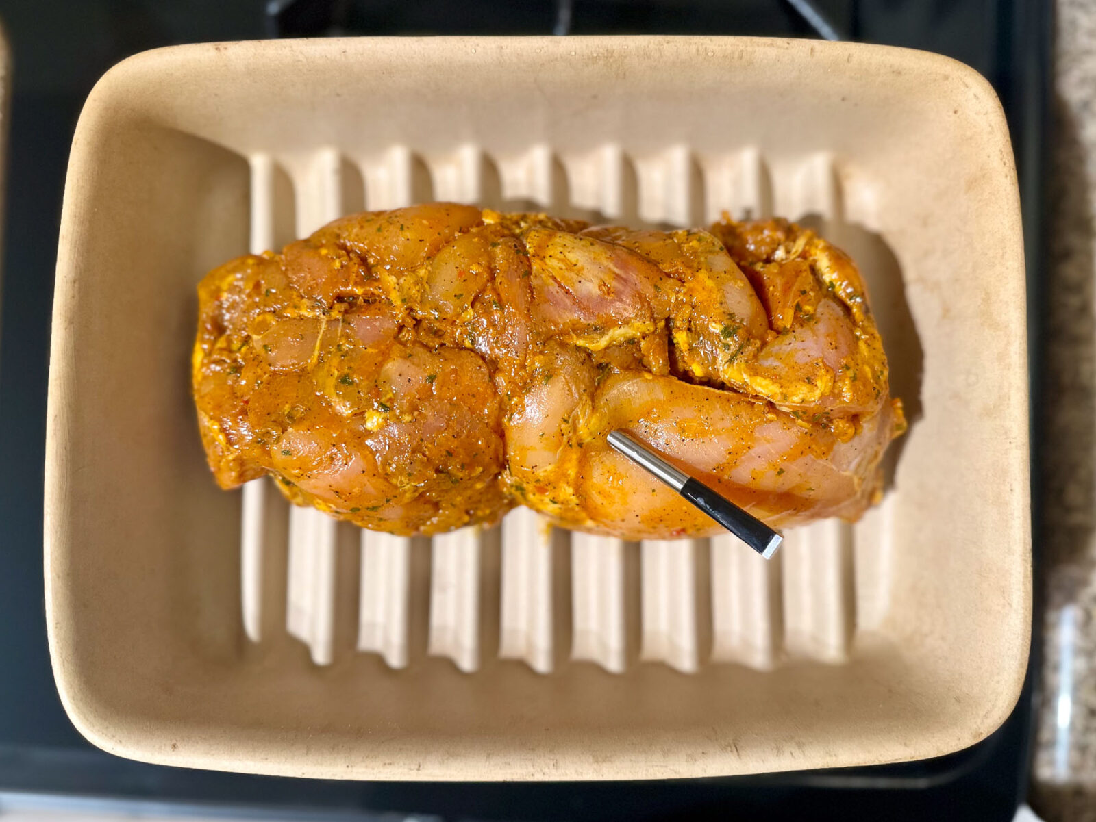 Trader Joe’s marinated chicken shawarma thighs on a grill pan with a meat thermometer inserted, ready to cook.