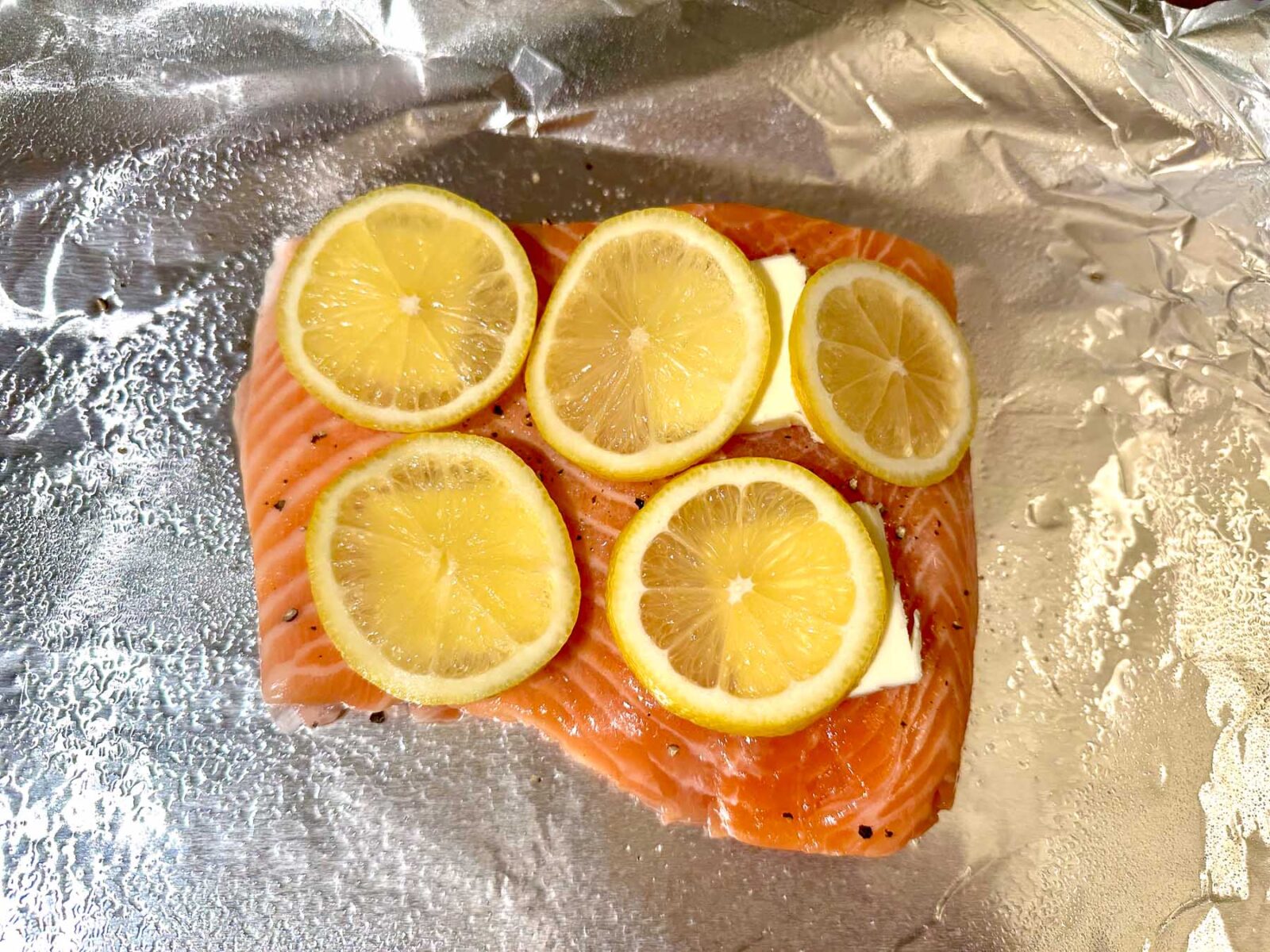 Salmon fillet on a foil-lined sheet pan, topped with lemon slices and butter, ready for roasting.