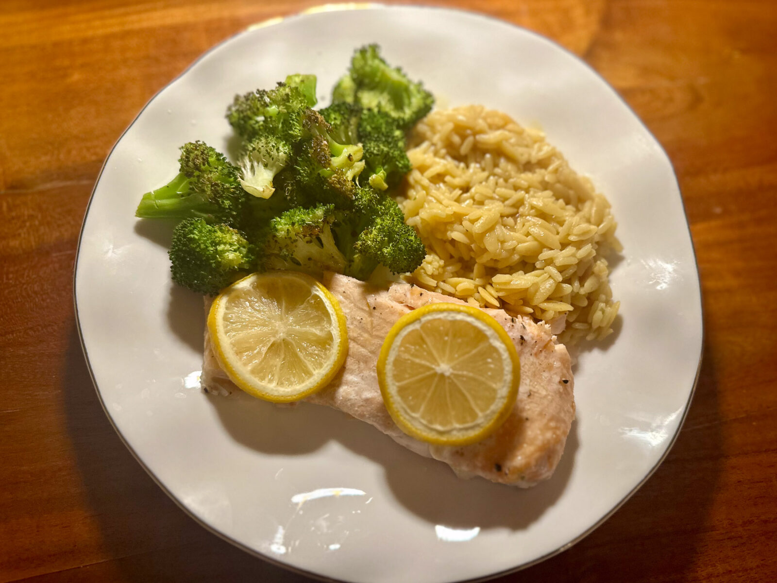 Plate of baked salmon topped with lemon slices, served with roasted broccoli and Trader Joe’s rice orzo pilaf.