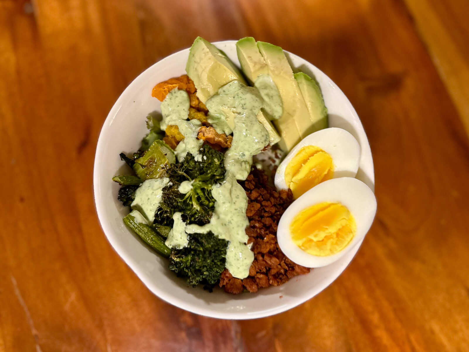 Soy chorizo bowl with roasted veggies, brown rice, avocado slices, soft-boiled eggs, and a drizzle of creamy cilantro aioli.