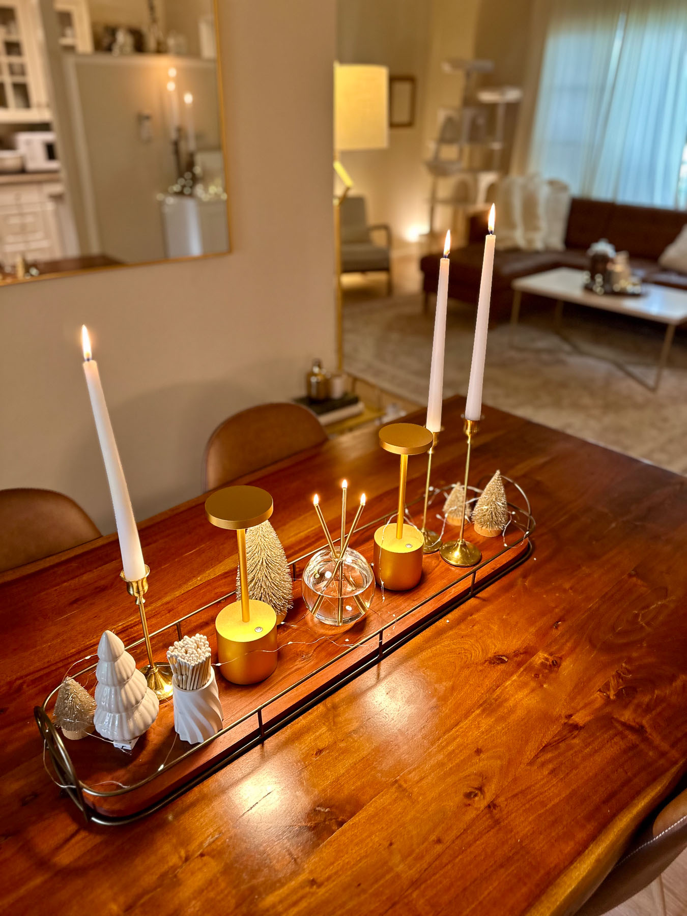 Dining table centerpiece with taper candles, gold candle holders, ceramic trees, and winter bottlebrush accents styled in a long tray.