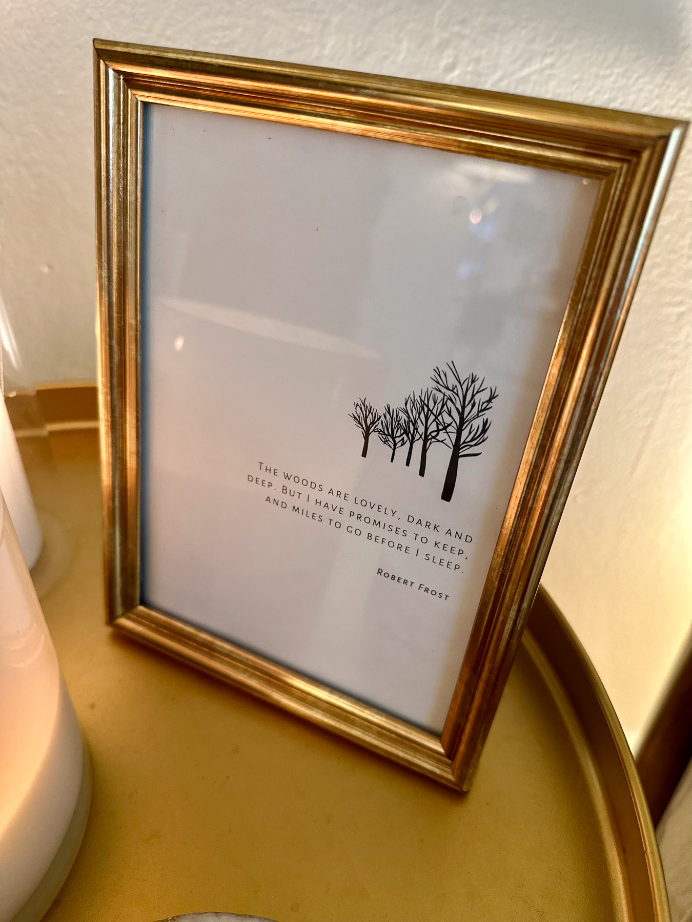 A simple and elegant display featuring a gold-framed print of a minimalist tree sketch and the Robert Frost quote, “The woods are lovely, dark and deep, but I have promises to keep, and miles to go before I sleep.” 