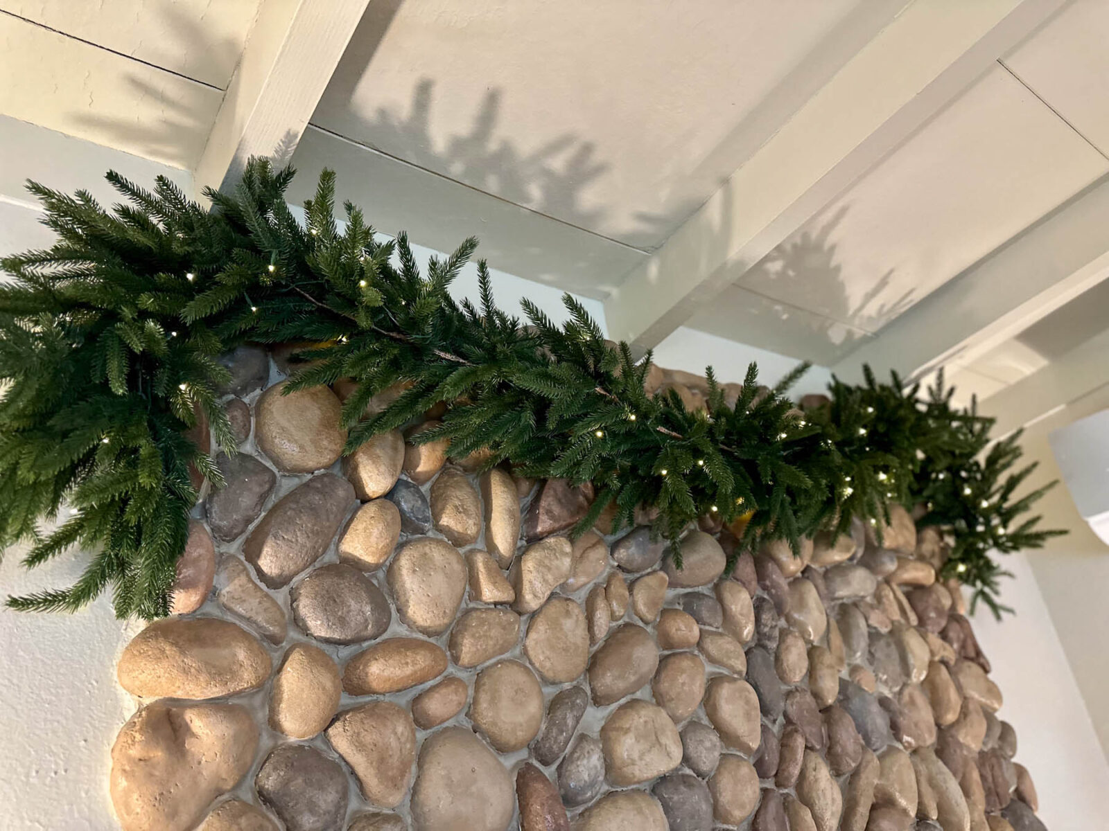 Green garland with fairy lights styled across a stone fireplace for a natural winter touch after the holidays.