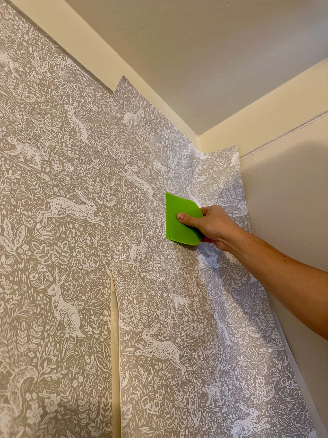 Smoothing peel-and-stick wallpaper in corner with a plastic bench scraper