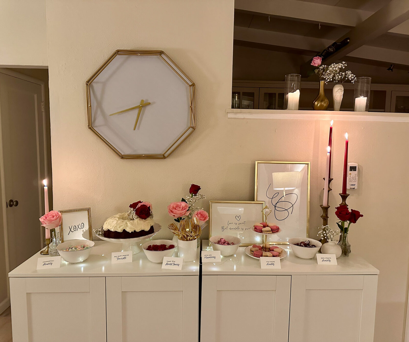 Galentine’s dessert table setup with a red velvet bundt cake, assorted candy, macarons, and framed signs, styled with taper candles and pink roses.