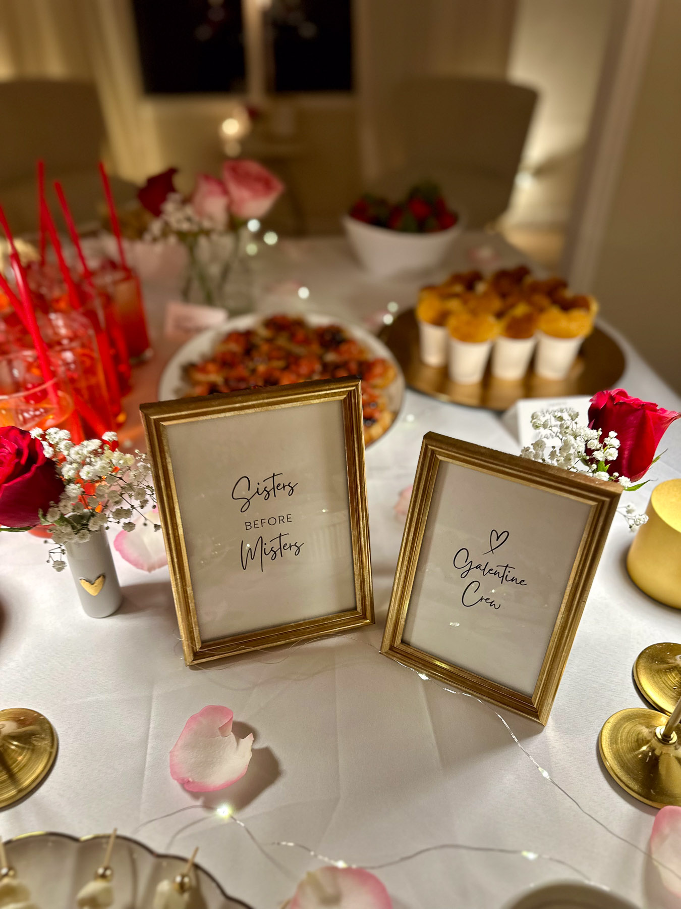 Framed Galentine’s quotes reading “Sisters Before Misters” and “Galentine Crew” displayed on a decorated party table with roses, snacks, and ambient lighting.