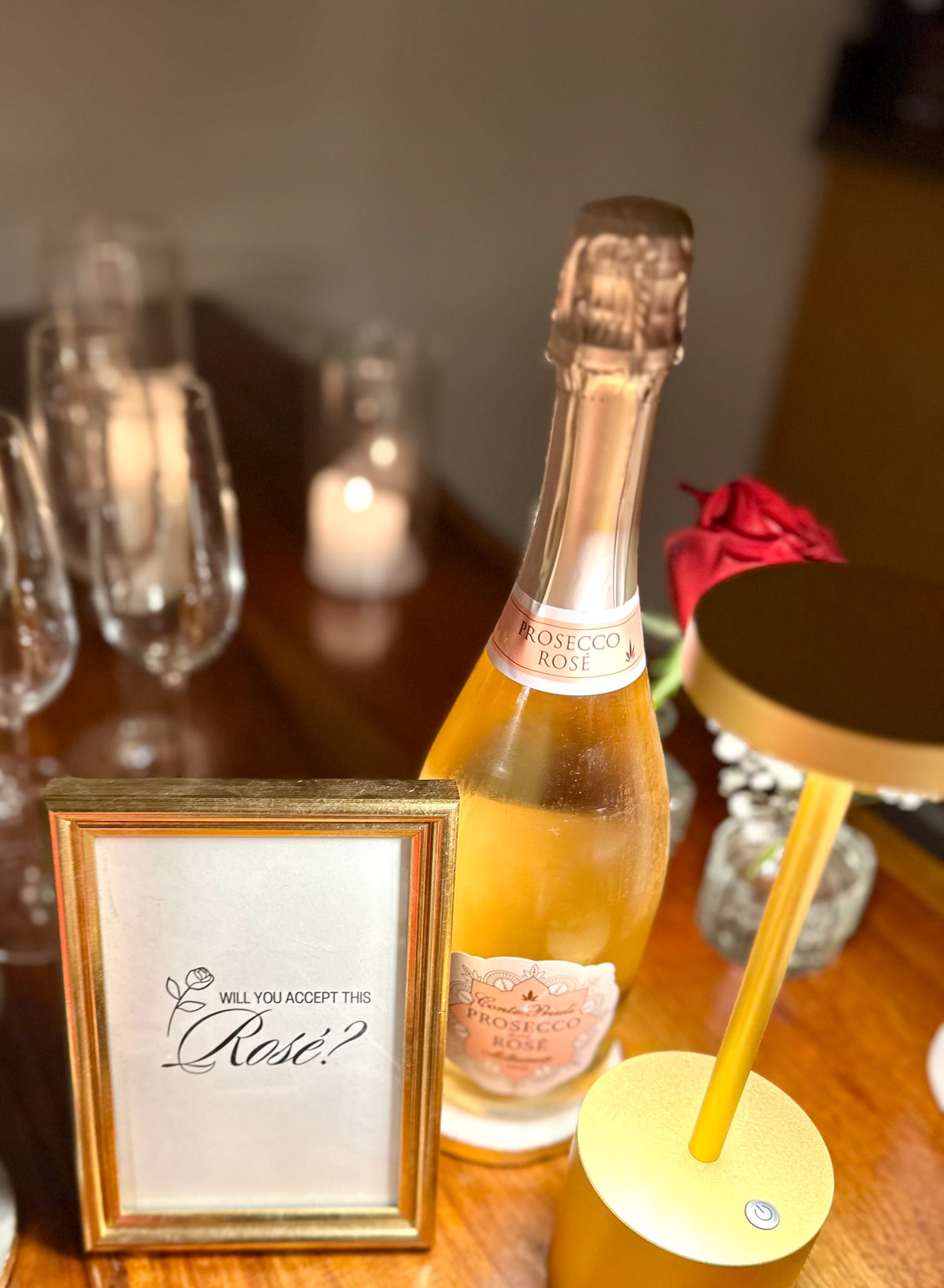 Sparkling rosé bottle with “Will you accept this rosé?” sign and gold lamp on a Bachelor watch party table