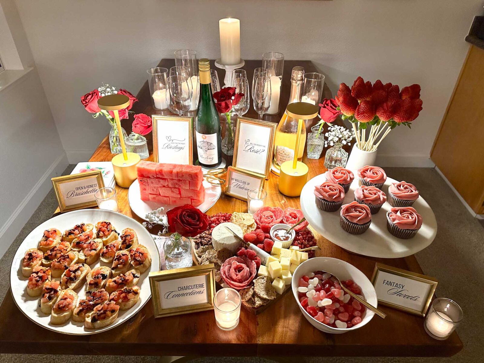 Bachelor watch party food spread with charcuterie board, cupcakes, bruschetta, candy, and rose-themed decor