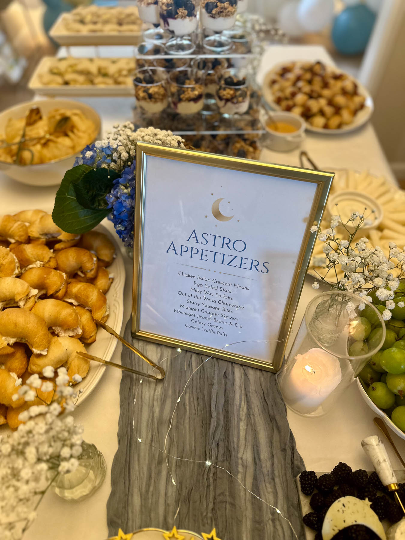 Baby shower food table with appetizers, candles, and moon-themed signage.
