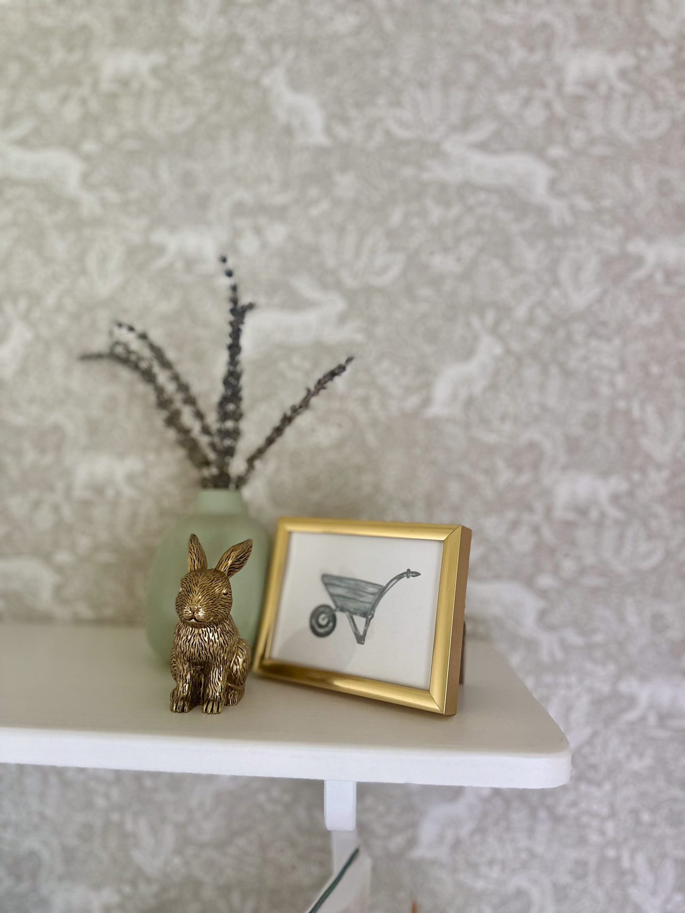 Gold bunny figurine, sage vase with dried lavender, and small framed wheelbarrow illustration styled as nursery shelf decor.