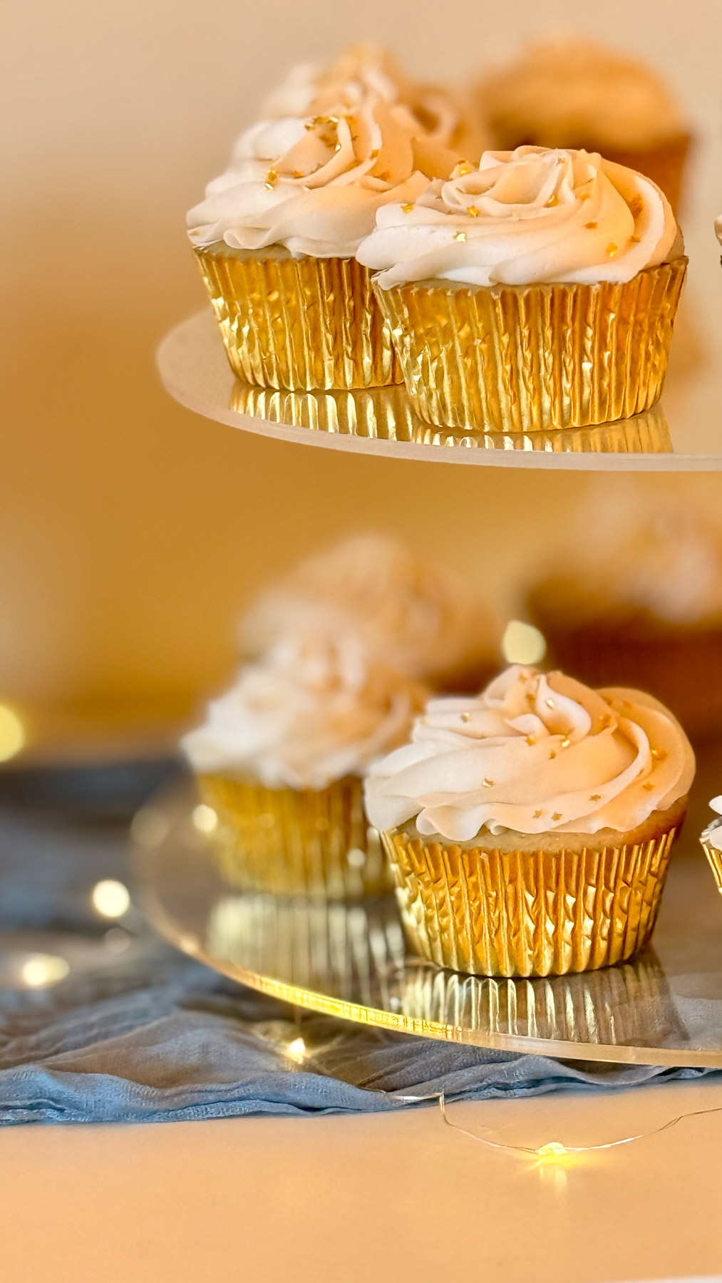 Gold-wrapped cupcakes with piped frosting and tiny gold star sprinkles for a baby shower dessert table