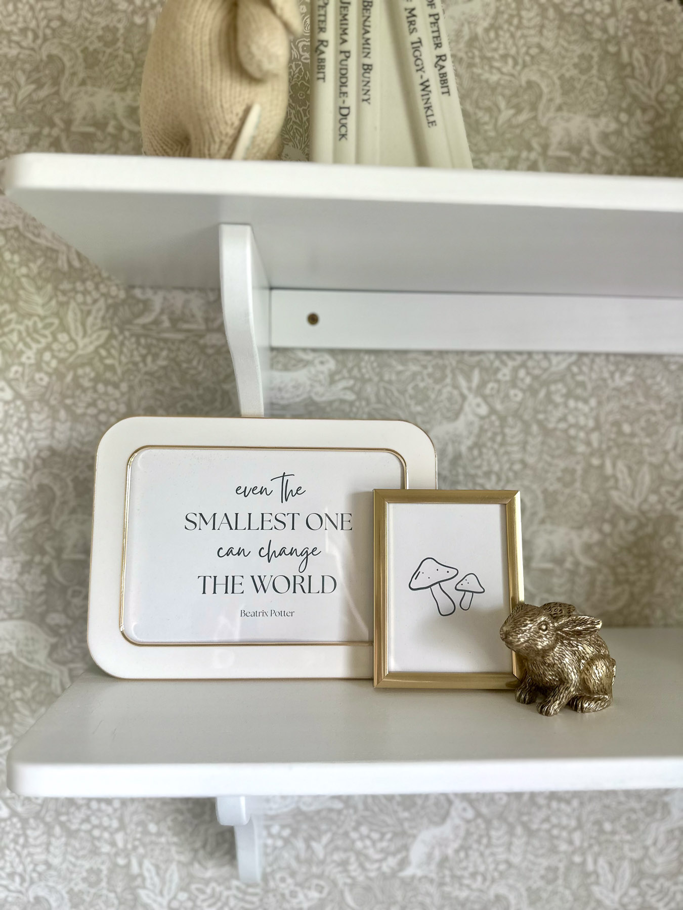Framed nursery quotes and small gold bunny figurine styled as white nursery shelf decor.