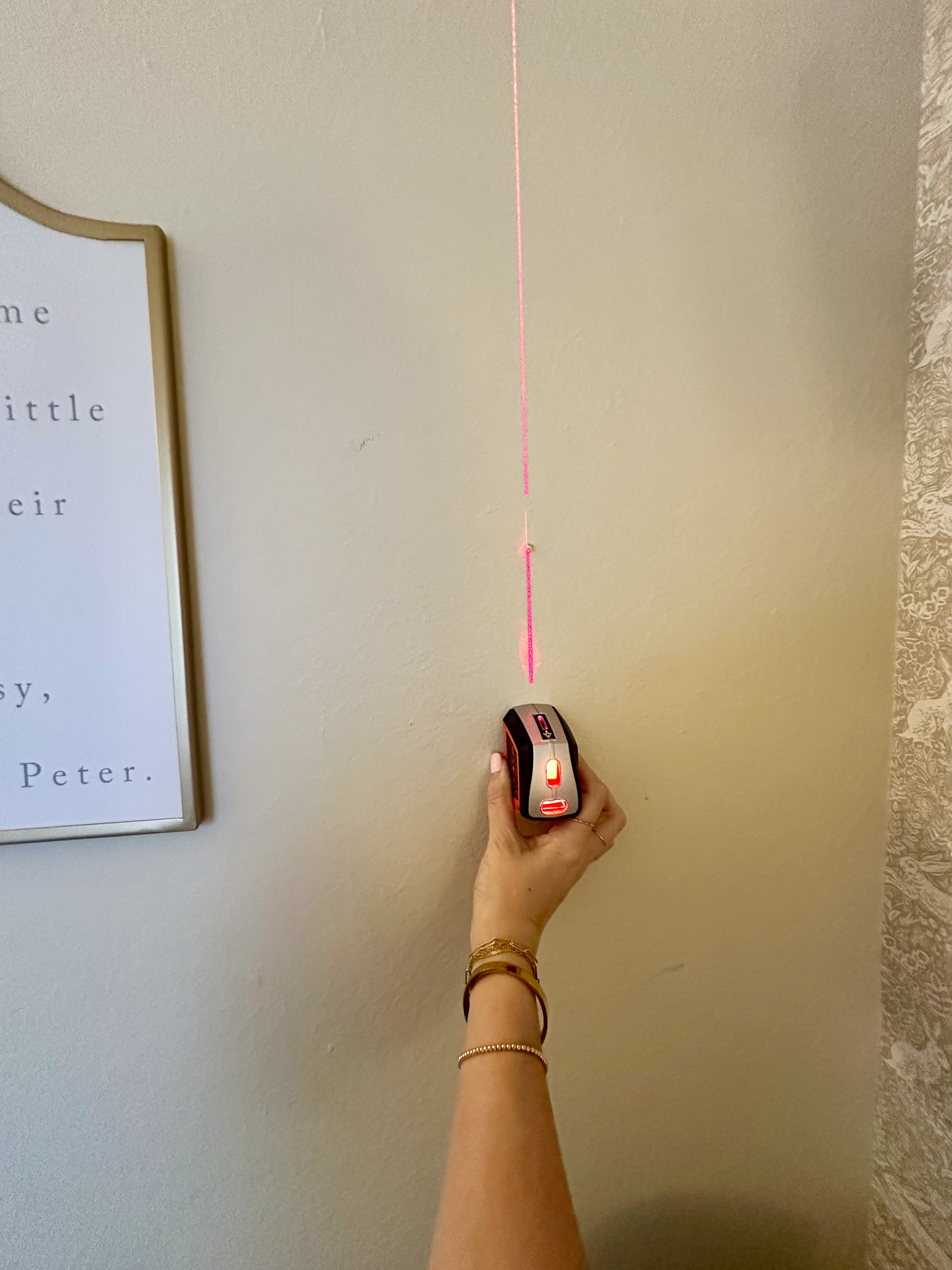 Using a laser level tool to align nursery wall decor before hanging framed prints.