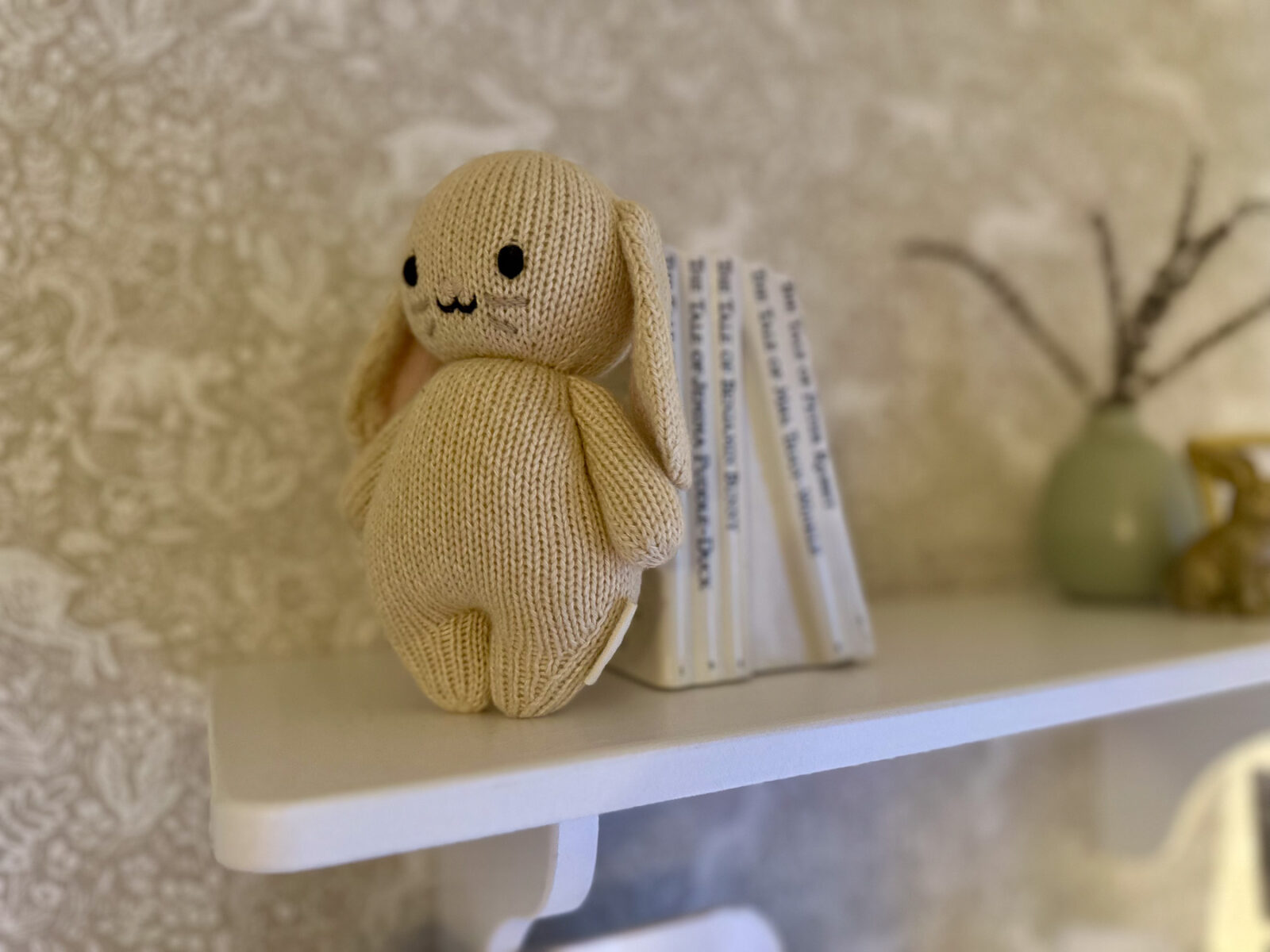 Cream knit bunny plush beside neutral books styled on white nursery shelf decor.