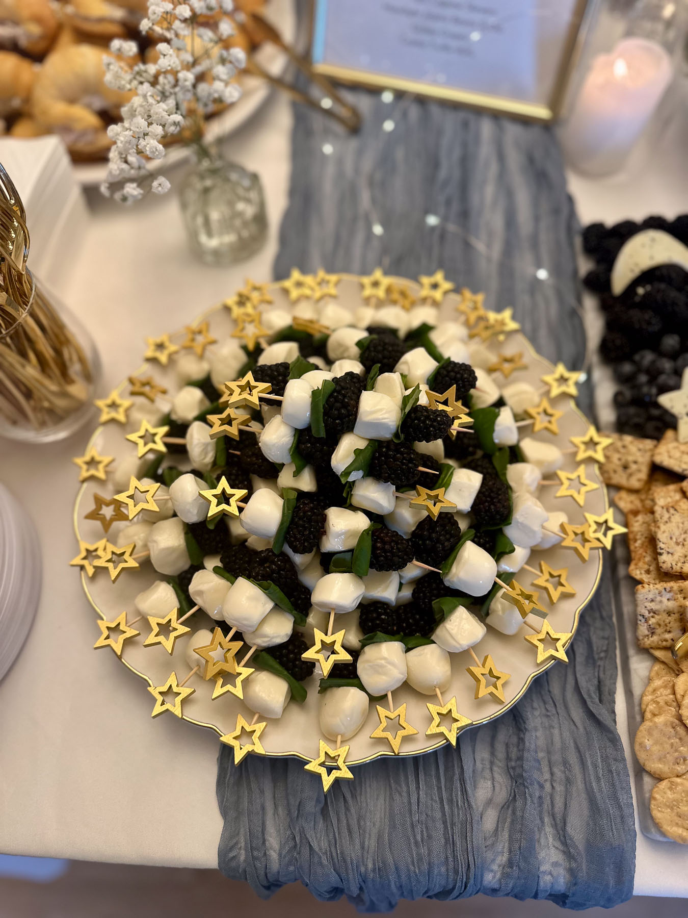Moon-themed baby shower snack platter with blackberry caprese skewers on gold star cocktail picks.