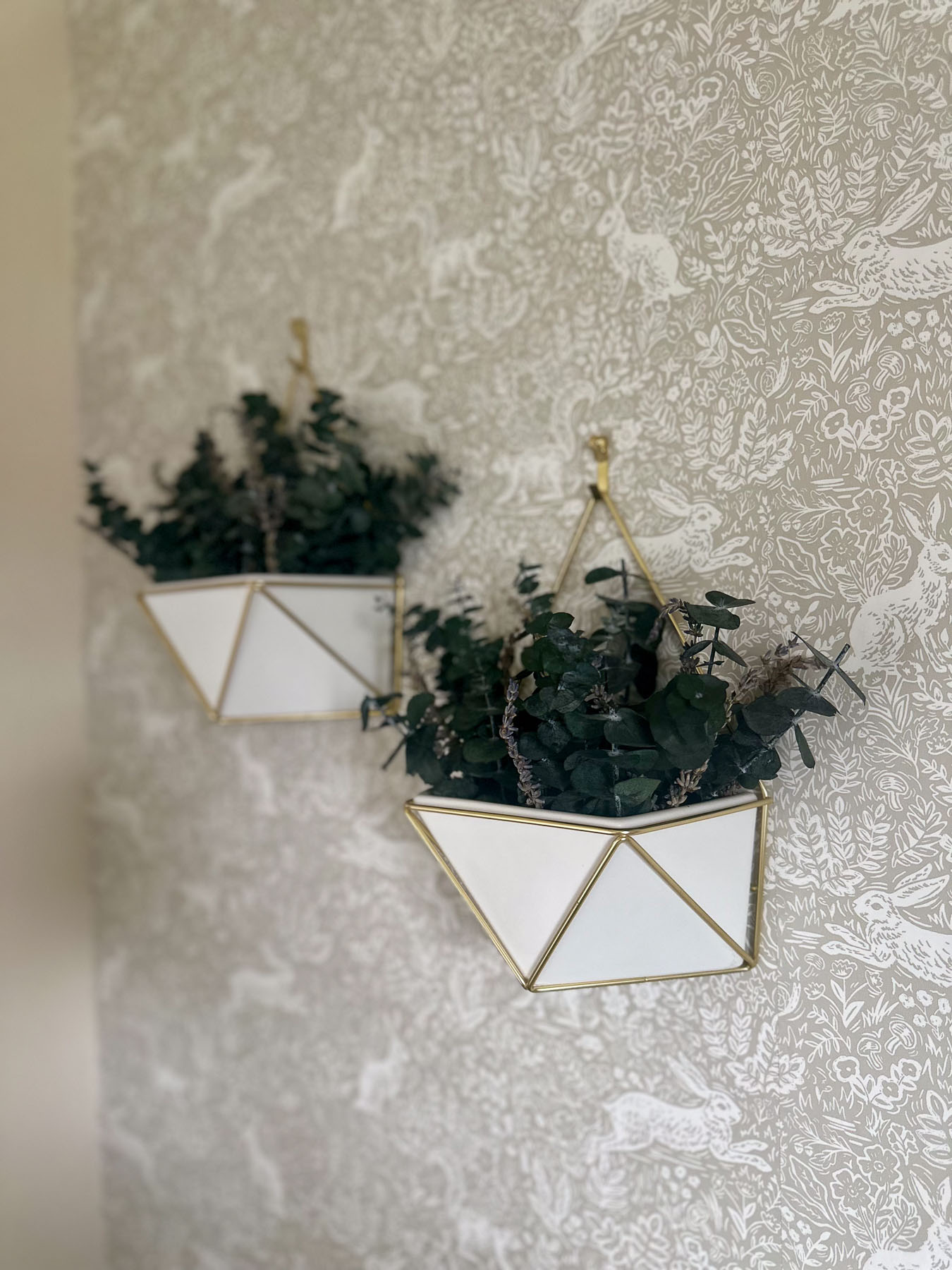 Gold geometric wall planters with greenery mounted on patterned wallpaper as nursery wall decor.