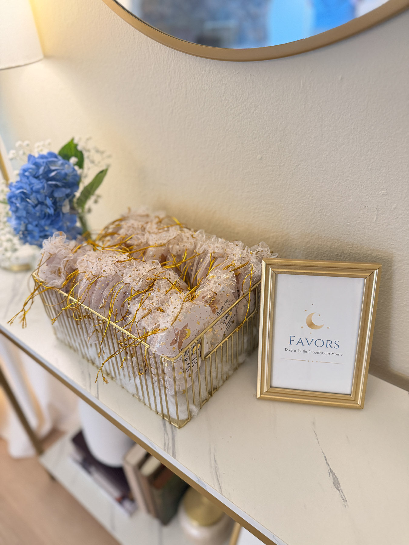 Baby shower favors displayed in a gold basket with moon-themed sign and hydrangeas
