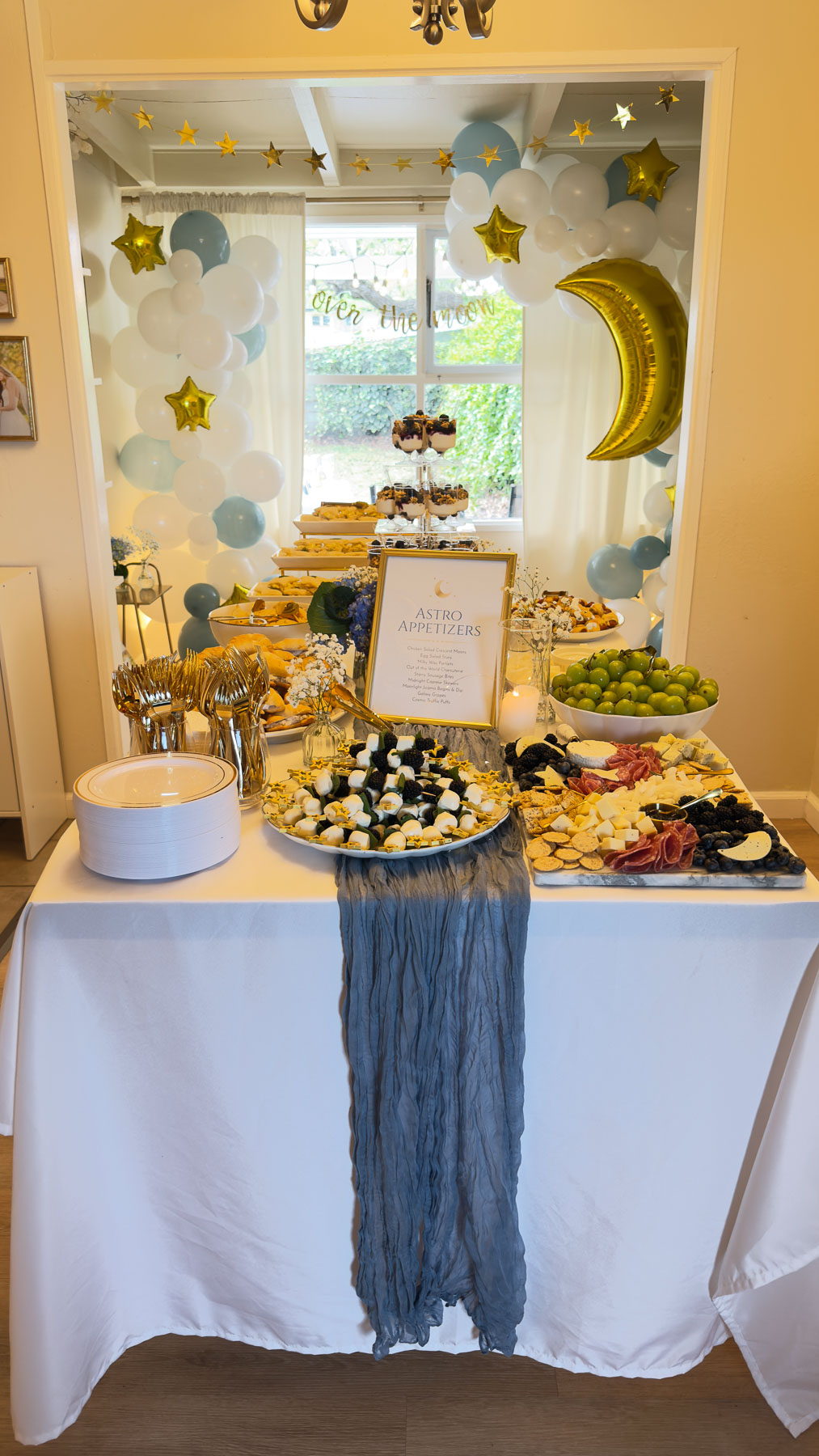 Over the Moon baby shower food table with balloon backdrop, charcuterie, and themed appetizers.