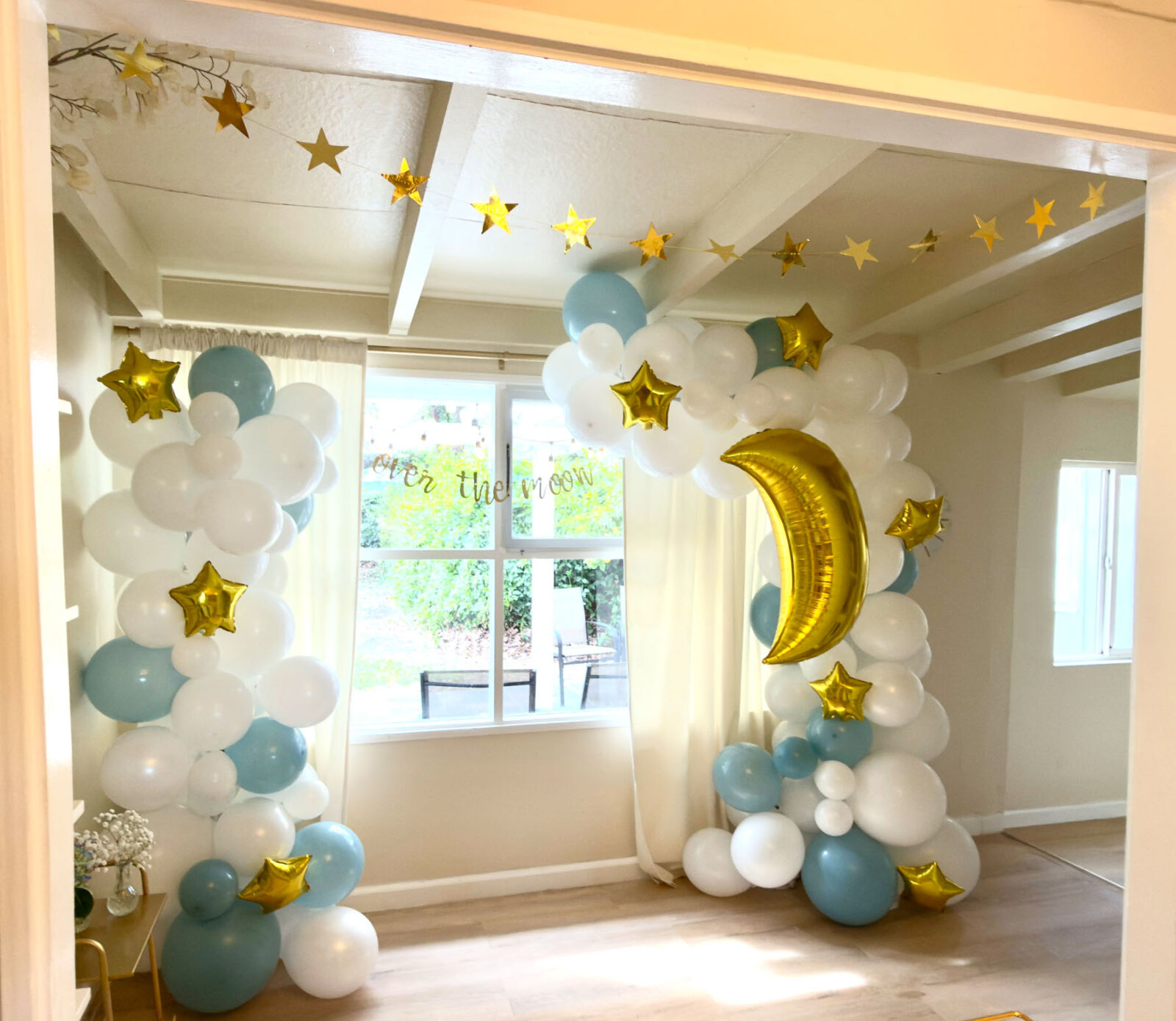 Over the Moon baby shower balloon arch with blue, white, and gold star decorations.