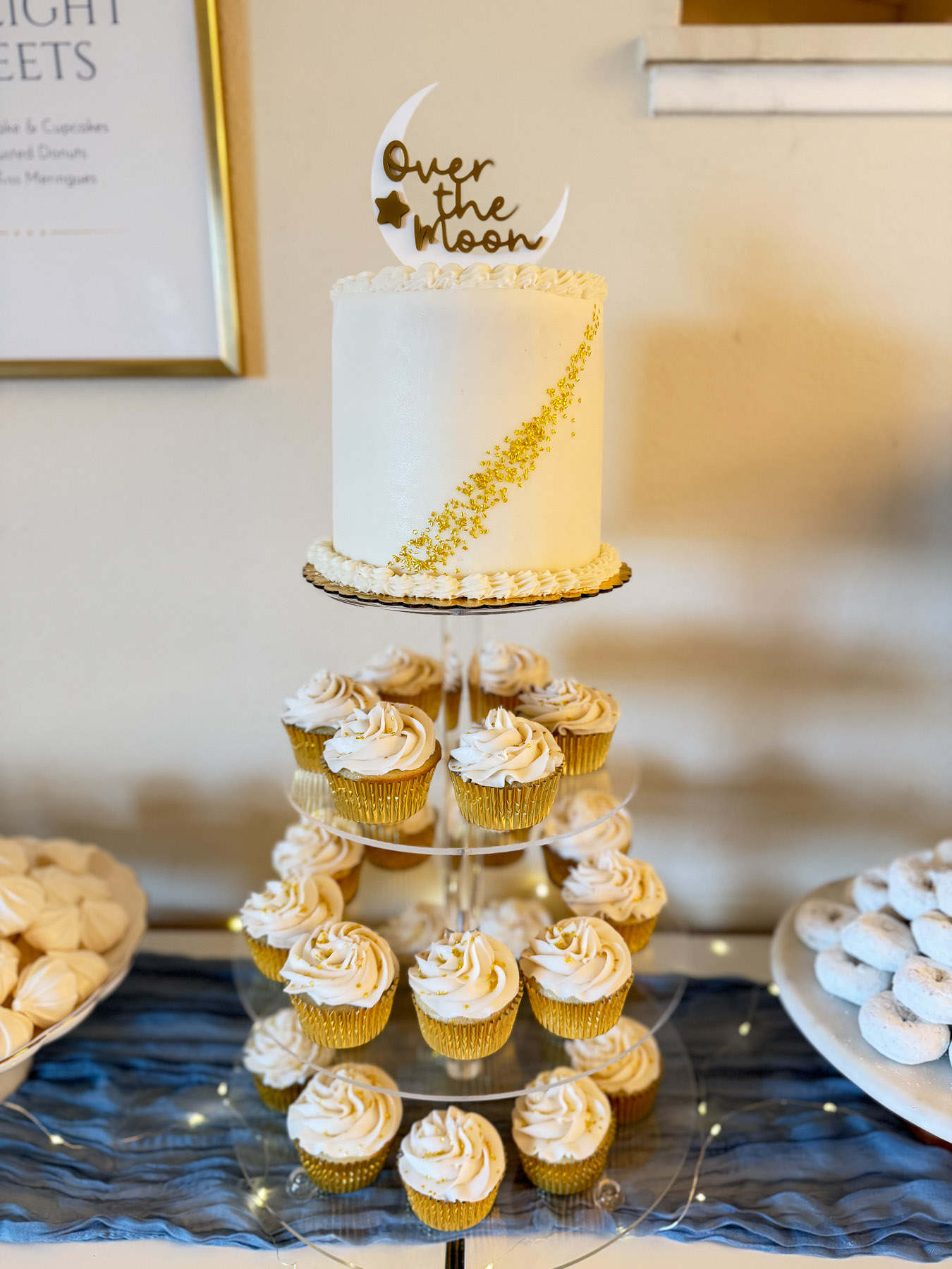 Over the Moon baby shower cake with gold detail and matching cupcakes display