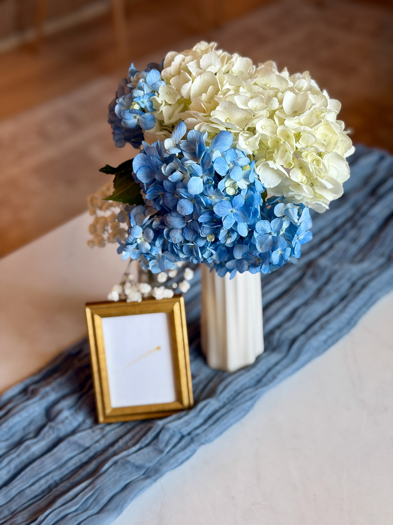 Blue and white hydrangea arrangement with gold frame and soft baby shower decor