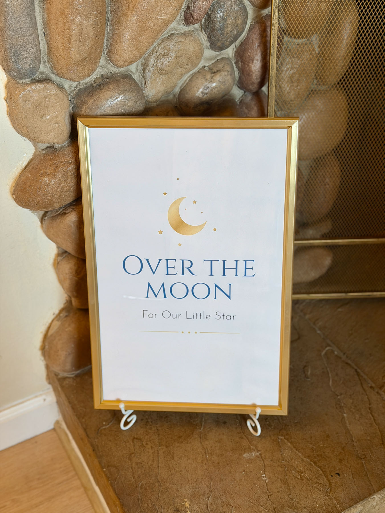 Baby shower sign with gold frame and soft neutral tones that reads "Over the Moon for Our Little Star"