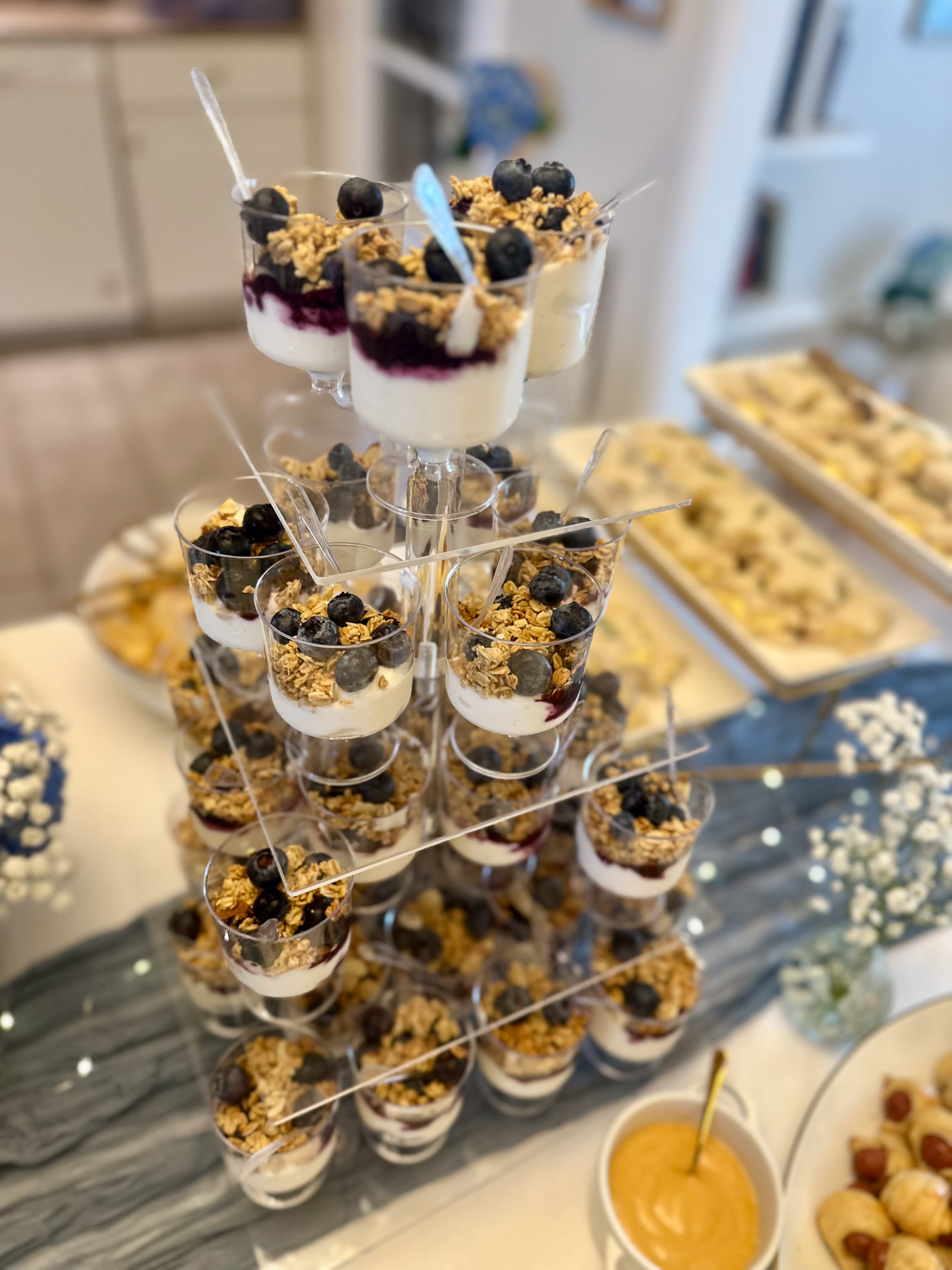 Mini yogurt parfait cups with blueberries and granola for a baby shower food table.