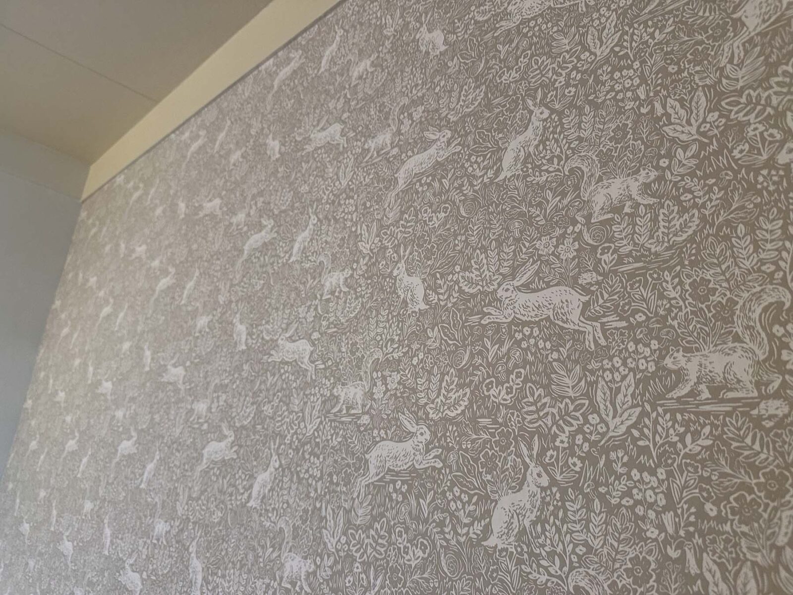 Soft neutral woodland wallpaper with rabbits and forest animals used as nursery wall decor.