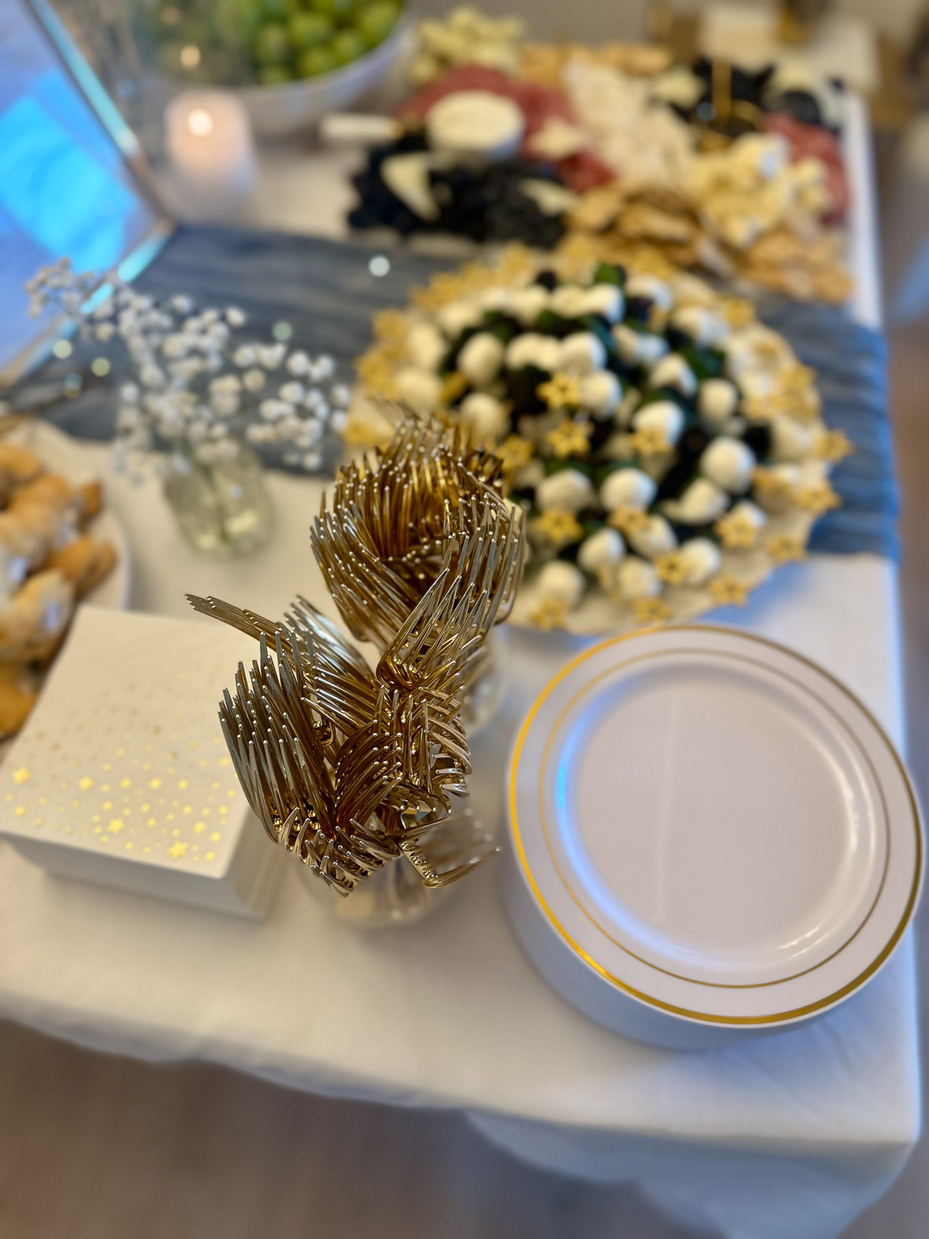 Table with appetizers, gold and white plates, gold forks, and gold star napkins for a party