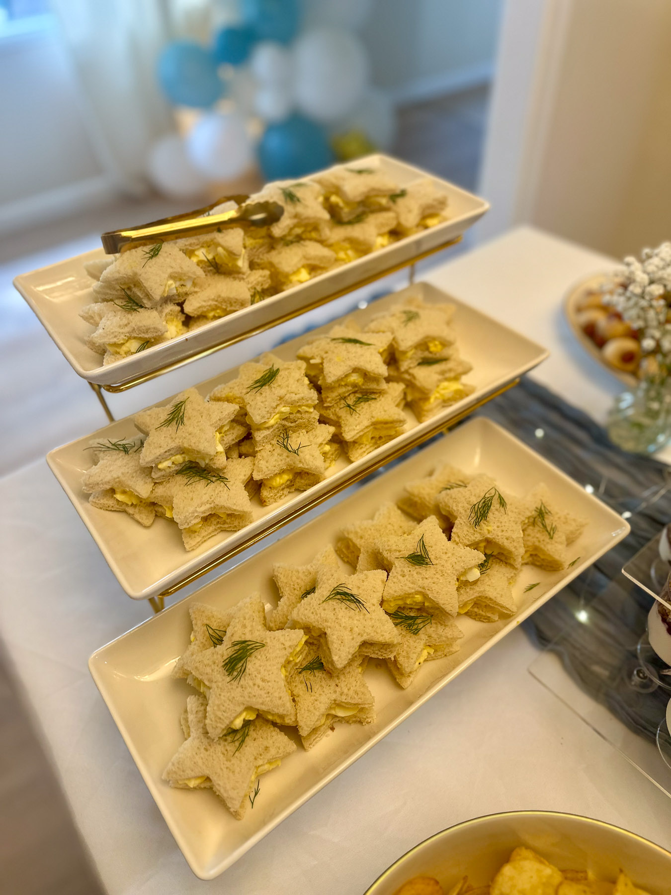Star-shaped tea sandwiches on tiered trays for a baby shower appetizer table
