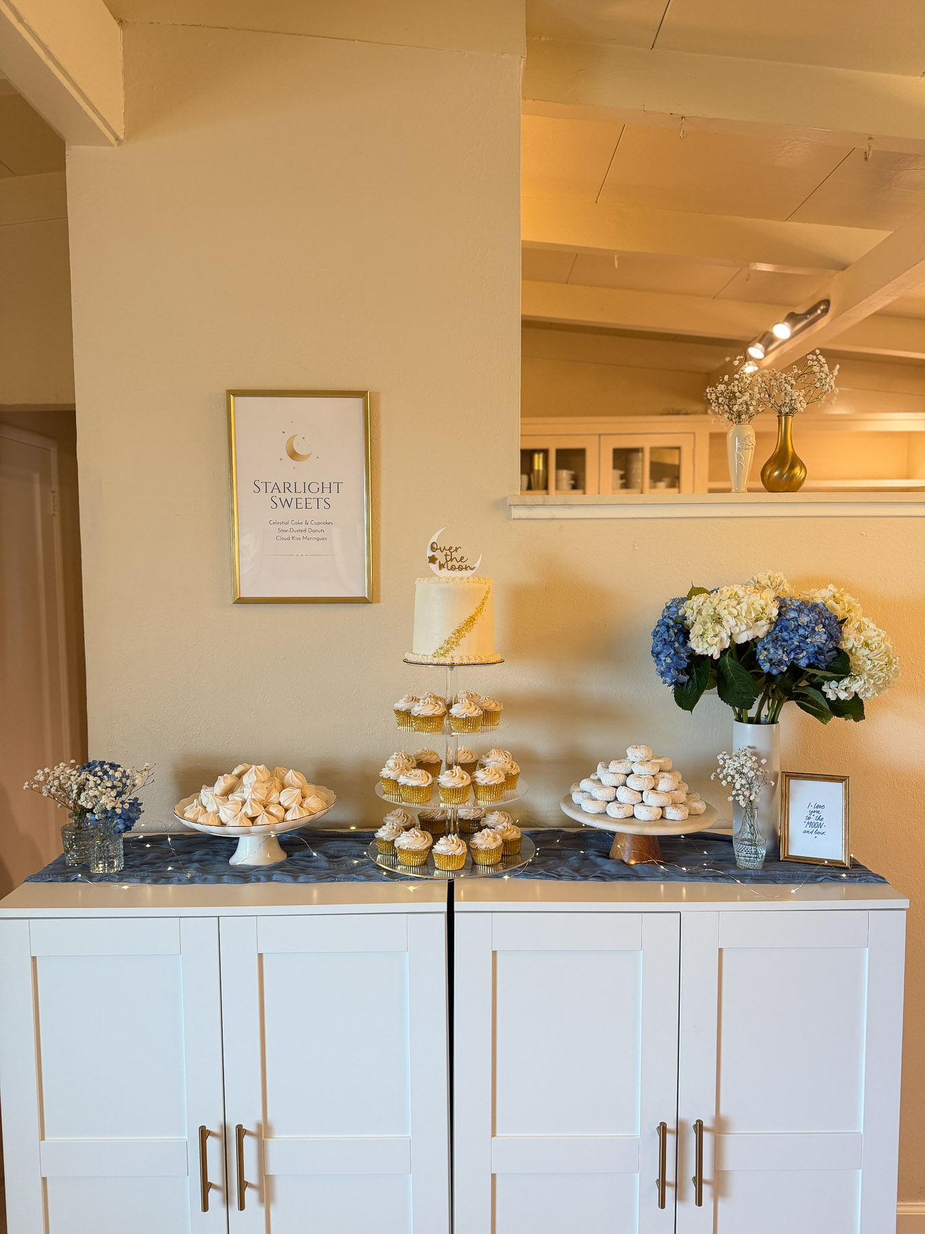 Over the Moon baby shower dessert table with cake, cupcakes, donuts, meringues, and blue hydrangeas