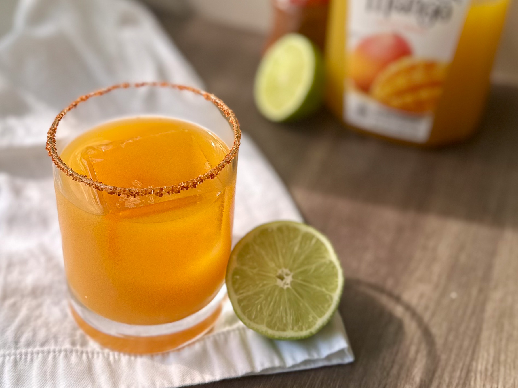 A refreshing virgin mango margarita from a list of easy mocktail recipes, featuring a Tajín rim, a large clear ice cube, and a cut lime.