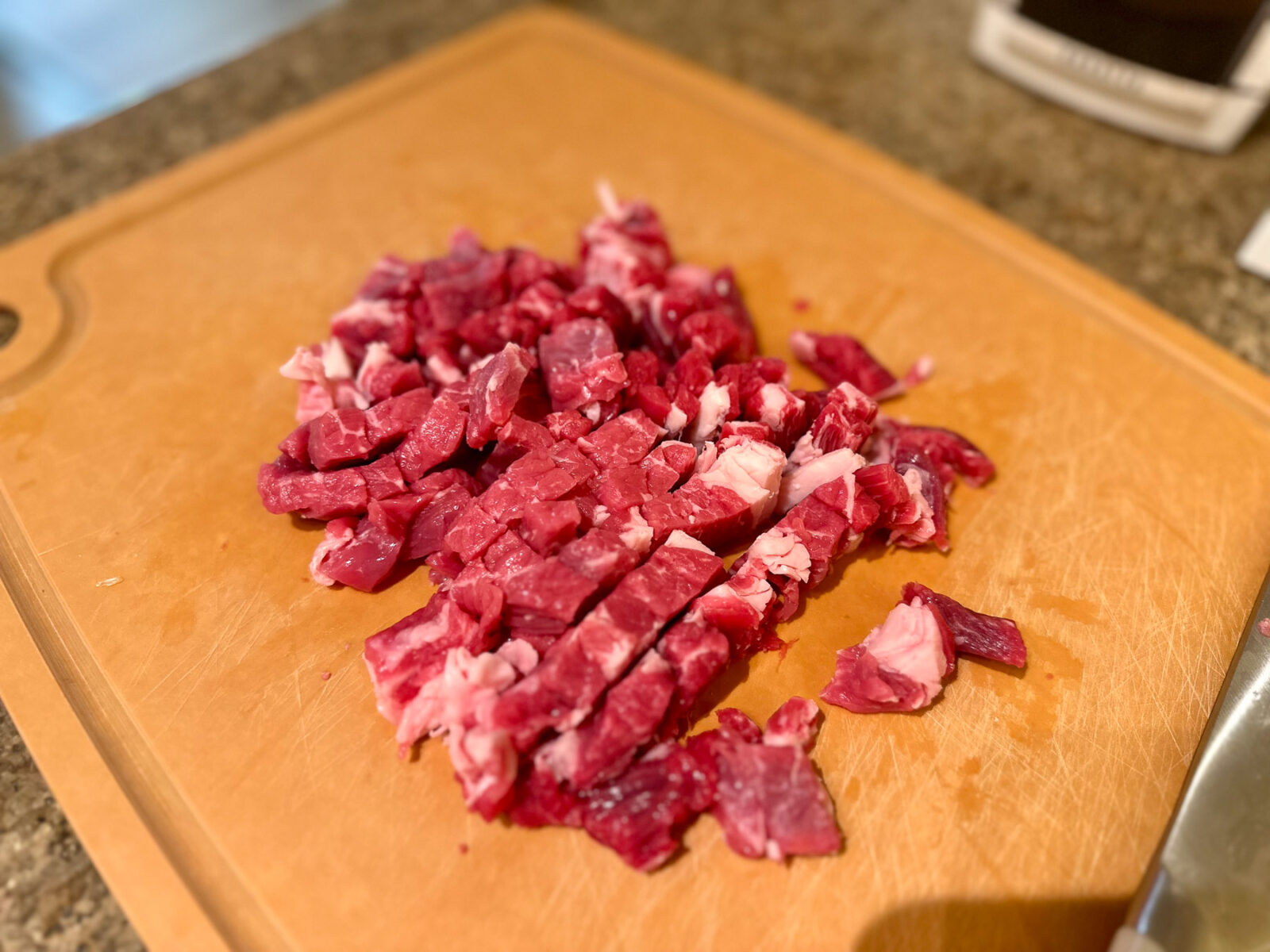 Raw ribeye steak chopped into small half-inch pieces on a wooden cutting board.