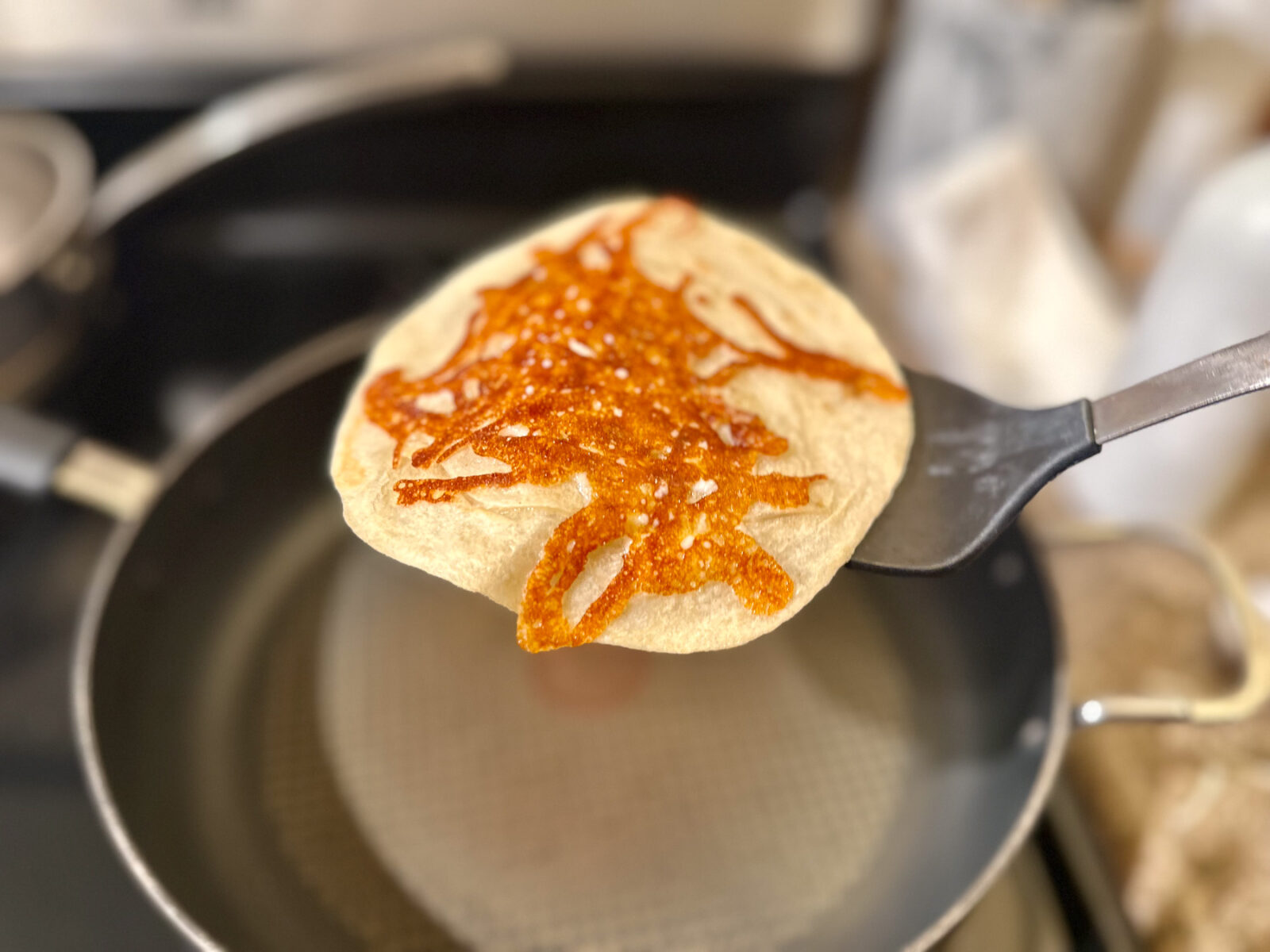A flour tortilla held up by a spatula showing a perfectly crispy, golden-brown mozzarella cheese crust on the bottom.