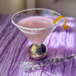 Lavender lemon drop martini with a light purple hue, sugar rim, and lemon twist garnish.