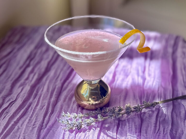 Lavender lemon drop martini with a light purple hue, sugar rim, and lemon twist garnish.