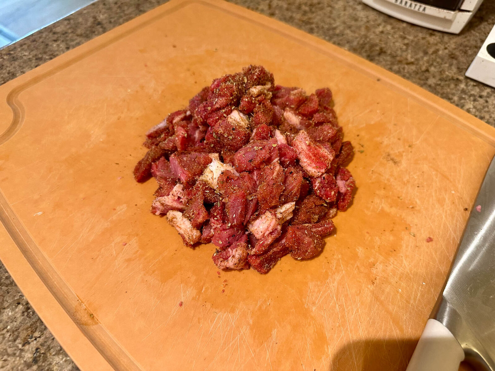 Chopped ribeye steak fully coated in oil and taco spice rub on a cutting board.