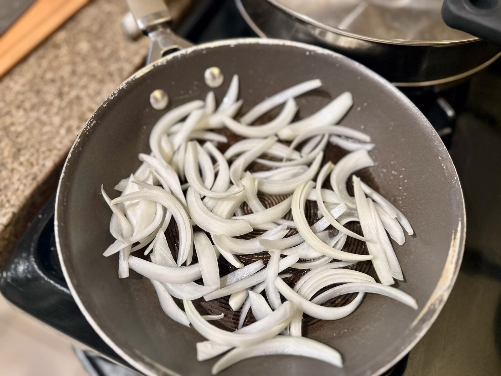 Sliced sweet onions in a skillet with oil before cooking.