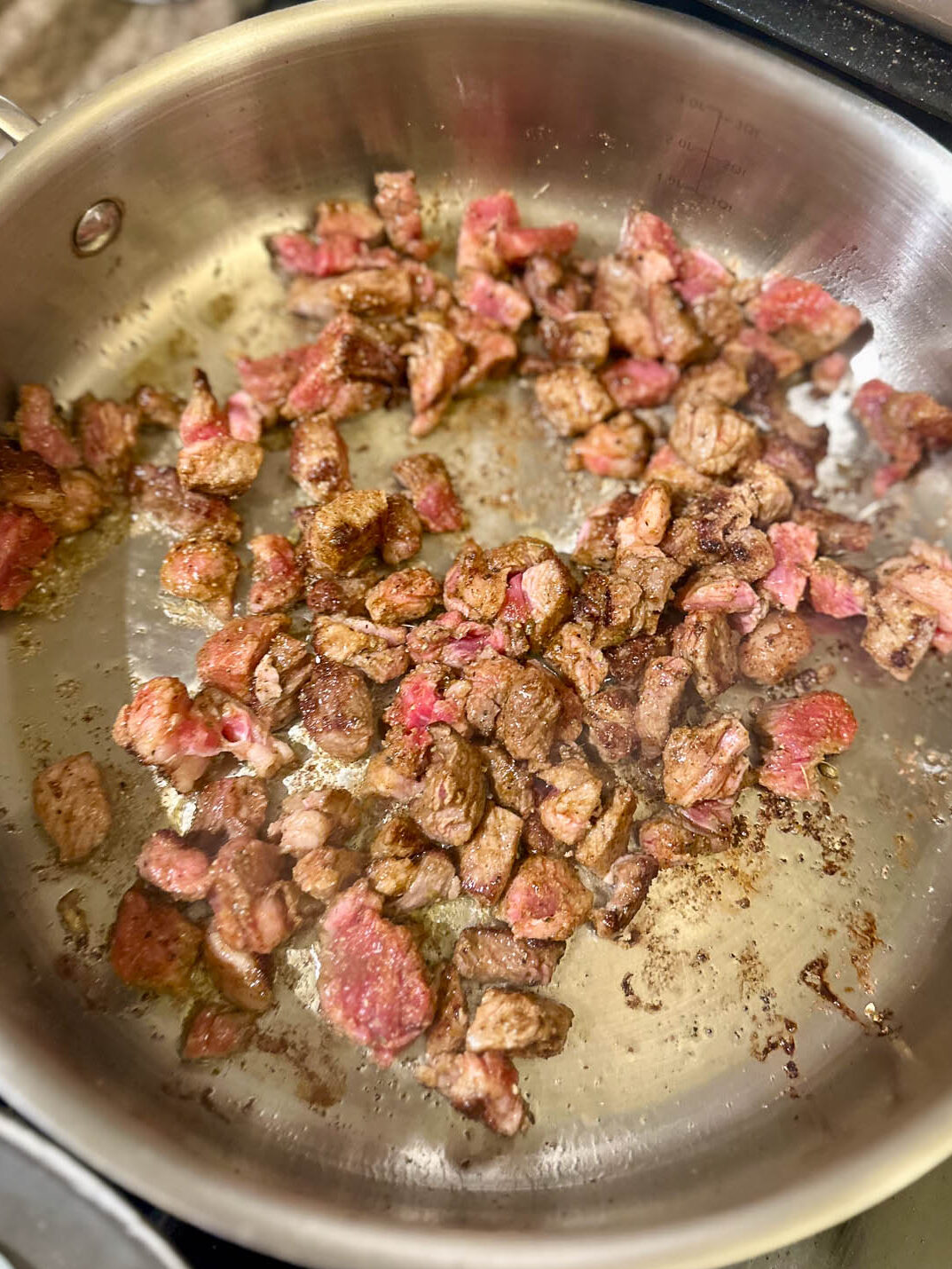 Ribeye steak pieces browning in a pan halfway through the cooking process.