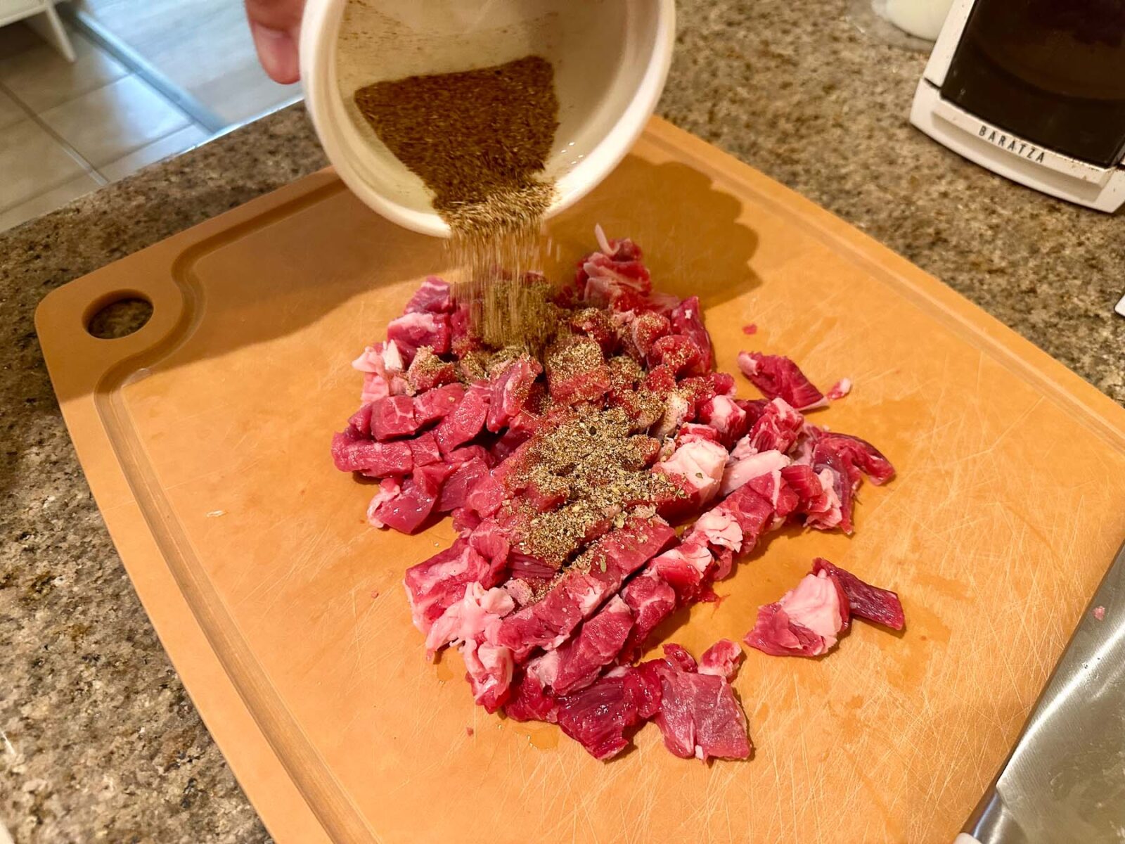 Pouring a dry spice rub from a small white bowl onto the chopped ribeye steak.