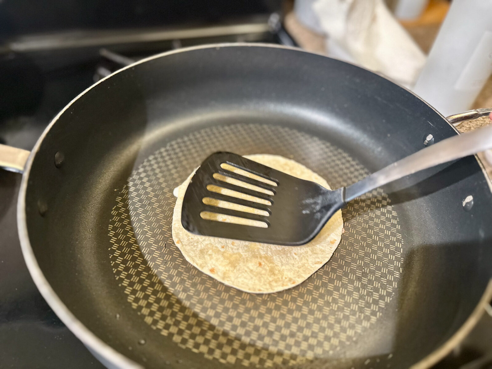 A flour tortilla being pressed down onto bubbling mozzarella cheese with a black spatula.
