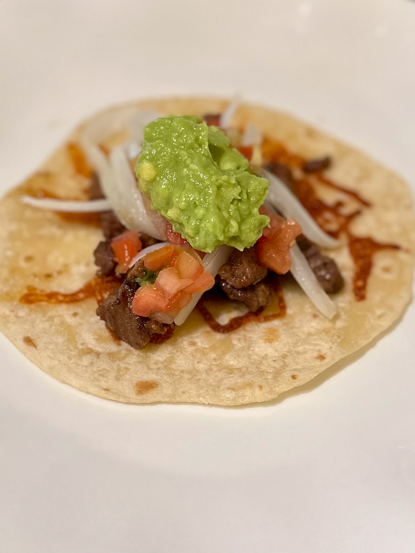 The final assembled taco with ribeye, onions, pico de gallo, and a scoop of fresh guacamole.