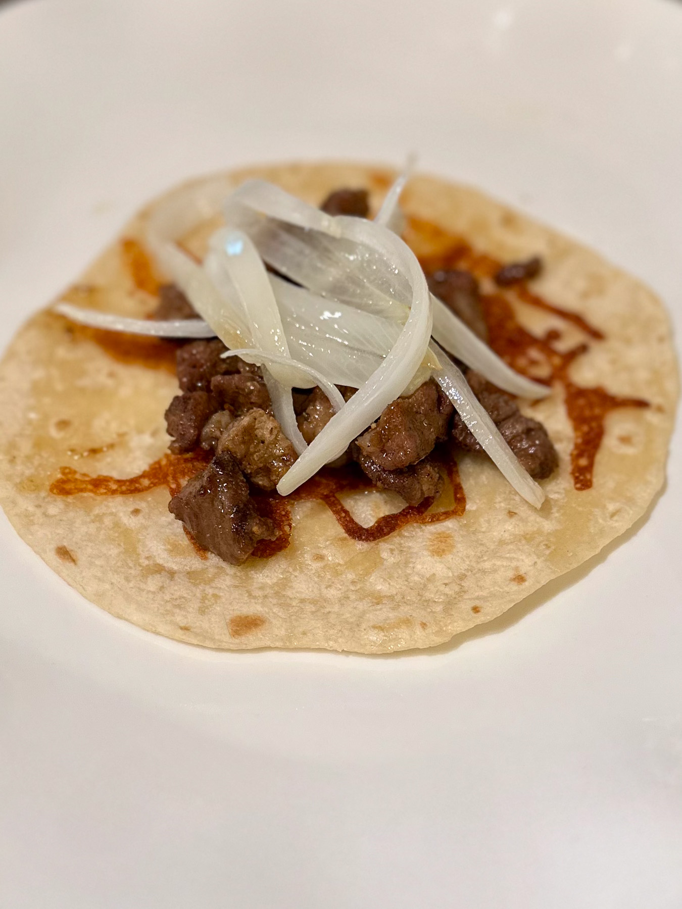 Adding sautéed sweet onions on top of the ribeye steak in the cheese-crusted tortilla.