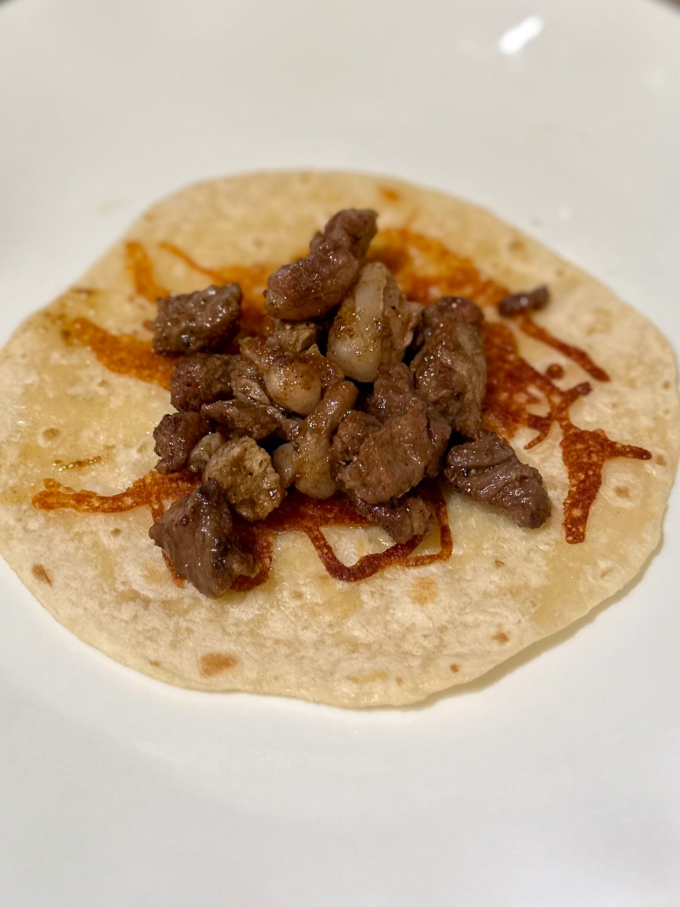 A cheese-crusted flour tortilla topped with a scoop of seared ribeye steak.