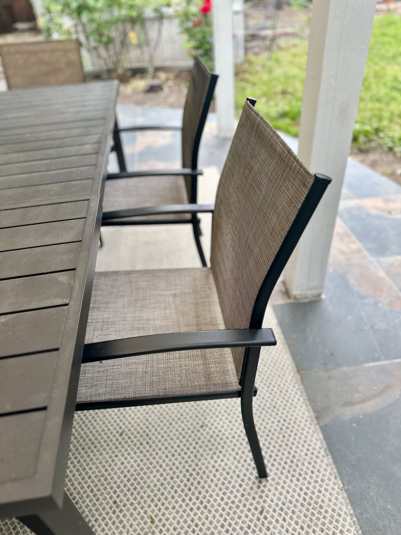 Close-up of brown mesh outdoor patio chairs tucked under a slatted dining table.