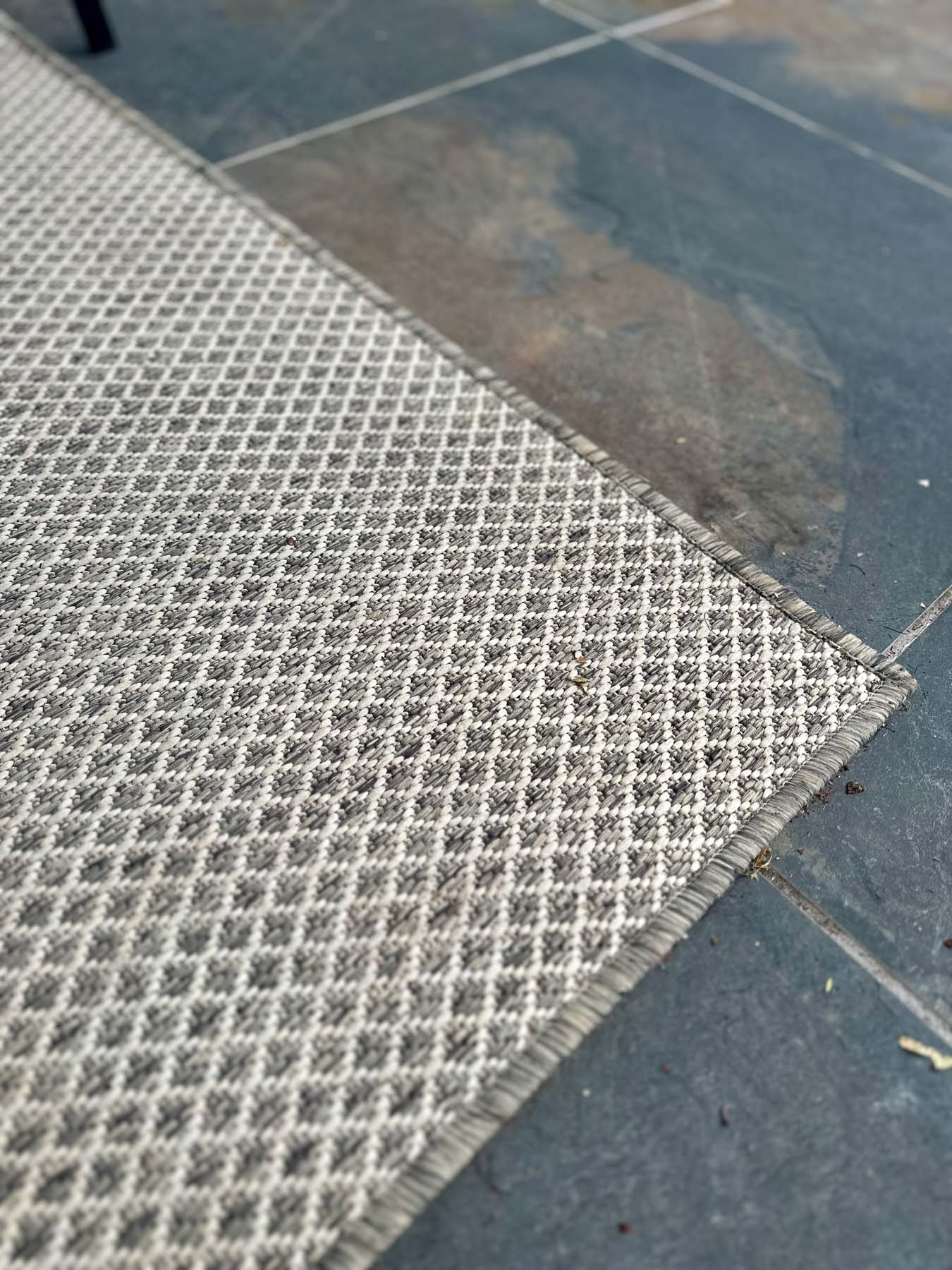 Close-up texture of a grey and white diamond patterned outdoor rug resting on a slate patio floor.